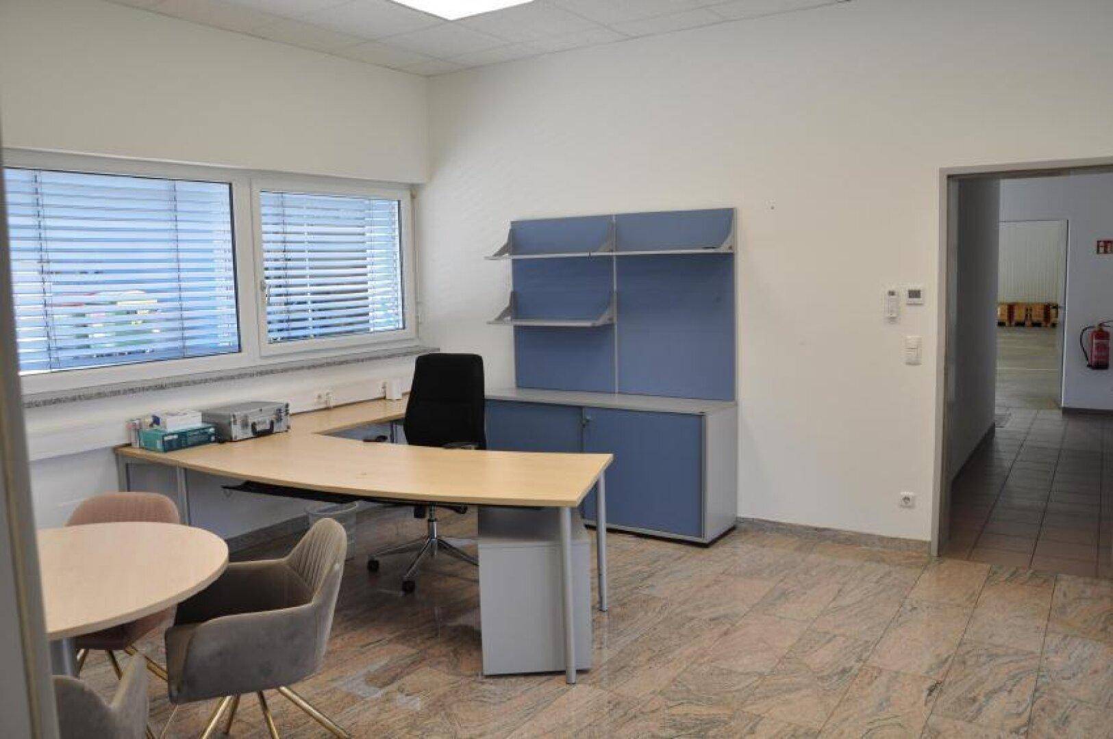 Funktionales Büro mit Schreibtisch, Bürostuhl und blauen Schränken, gut beleuchtet durch Fenster.