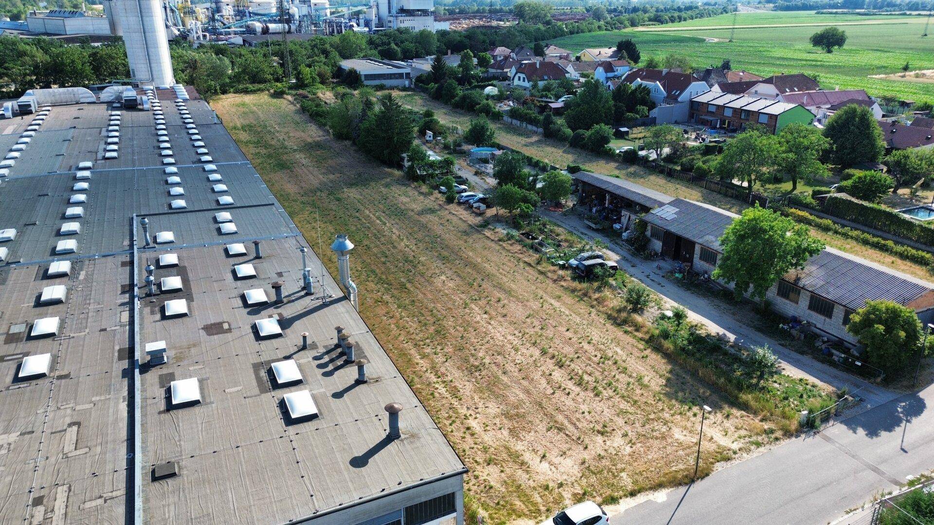 Weitläufige Luftansicht eines Industriegebäudes, eines freien Grundstücks und angrenzender Wohnsiedlung.