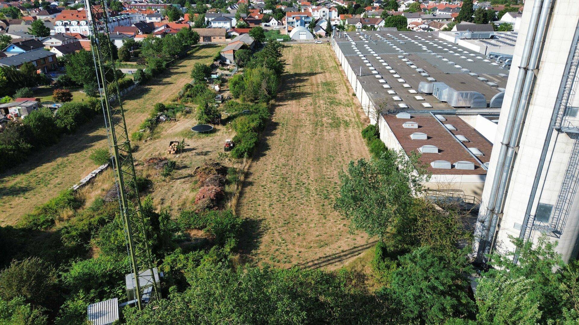 Panoramablick aus der Luft auf ein unbebautes Grundstück zwischen Industrie und Wohngebiet.