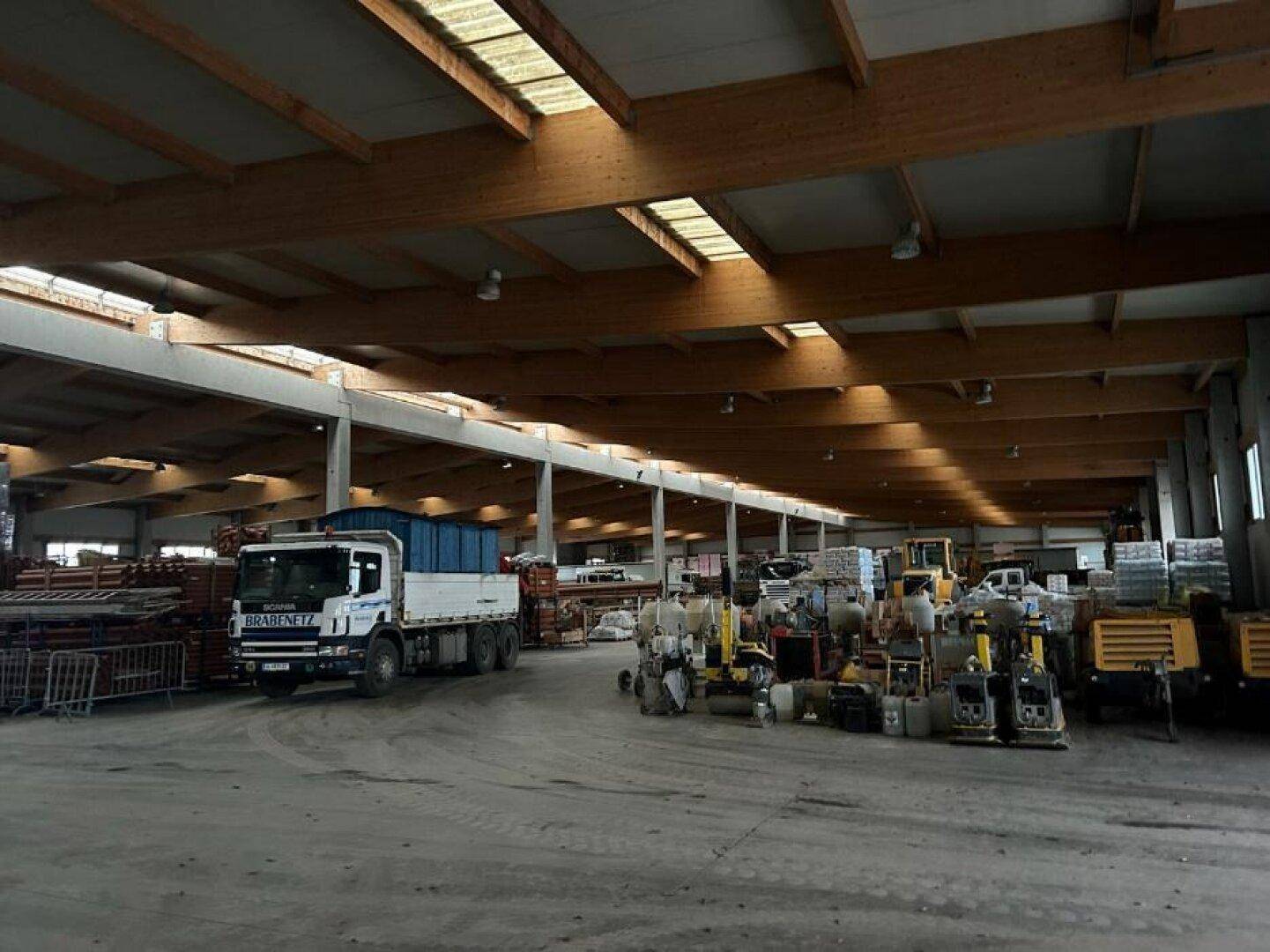 Geräumige Lagerhalle mit hohen Holzdecken, Oberlichtern und Betonboden, gefüllt mit Maschinen und einem LKW.