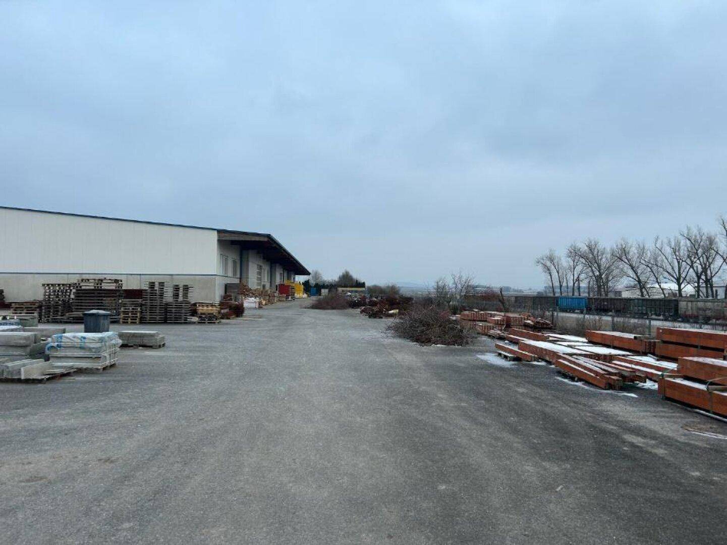 Weitläufiger gepflasterter Hofbereich vor der Lagerhalle mit verschiedenen Baumaterialien und Paletten im Freien.