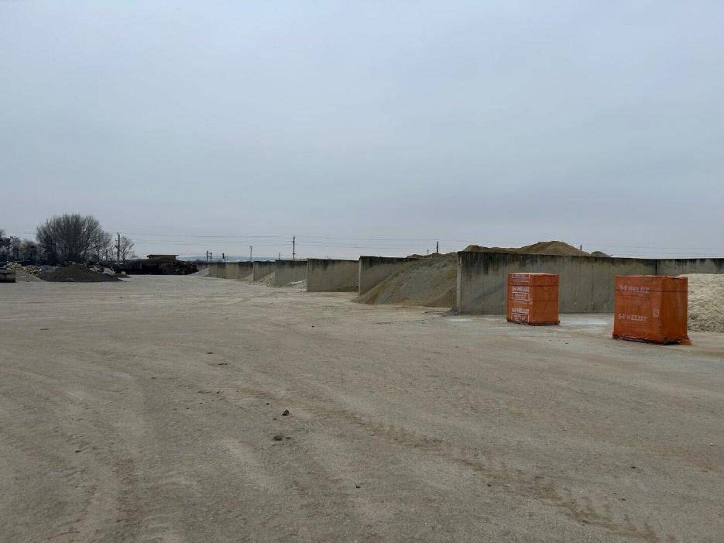 Großer Freilagerbereich mit Betonwänden zur Trennung von Schüttgütern und gestapelten Materialien unter bewölktem Himmel.