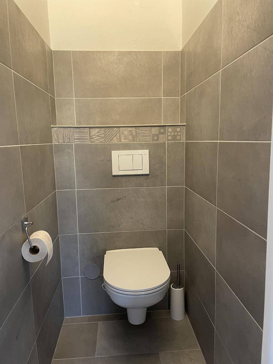 Separates WC mit wandhängender Toilette und modernen grauen Fliesen.