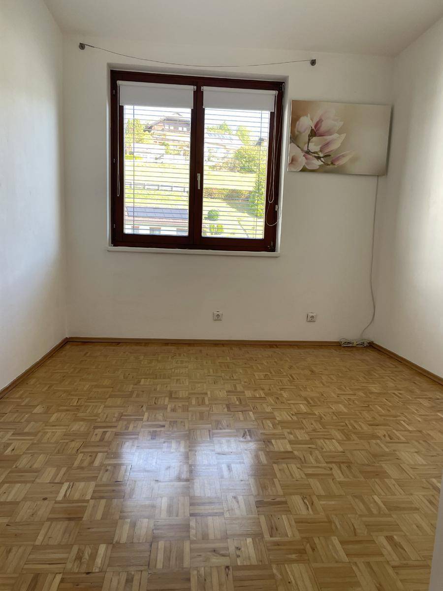 Helles Schlafzimmer mit Parkettboden und Fenster mit Blick ins Grüne.