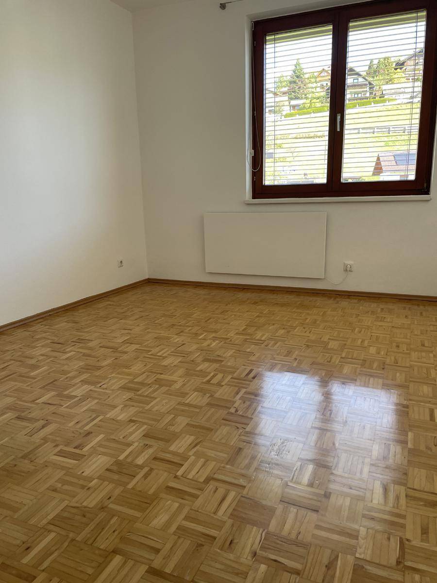 Leeres Zimmer mit Parkettboden, großem Fenster und Heizkörper.