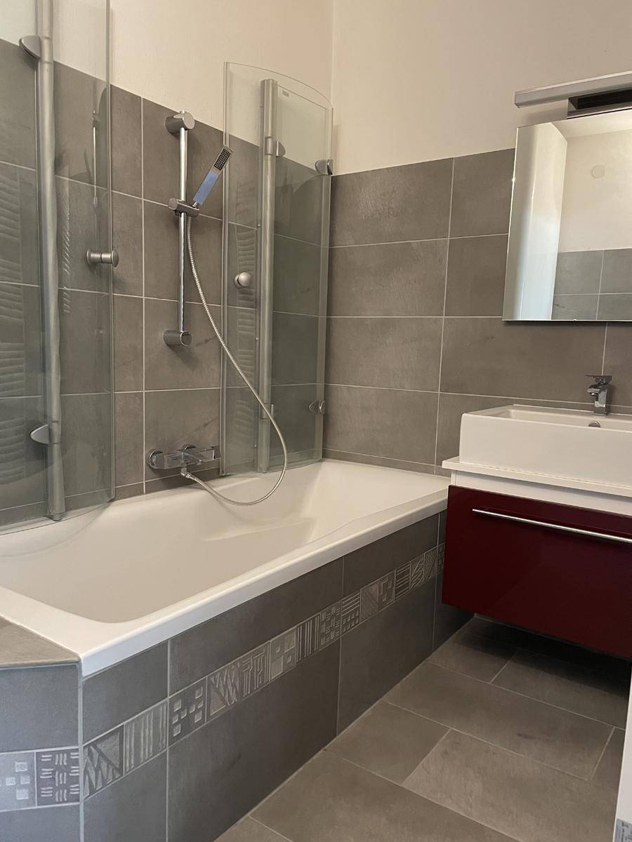 Modernes Badezimmer mit Badewanne, Duschabtrennung und grauen Fliesen.