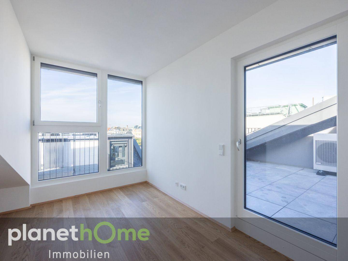 Lichtdurchfluteter Raum mit Holzboden und Zugang zu einer Dachterrasse.
