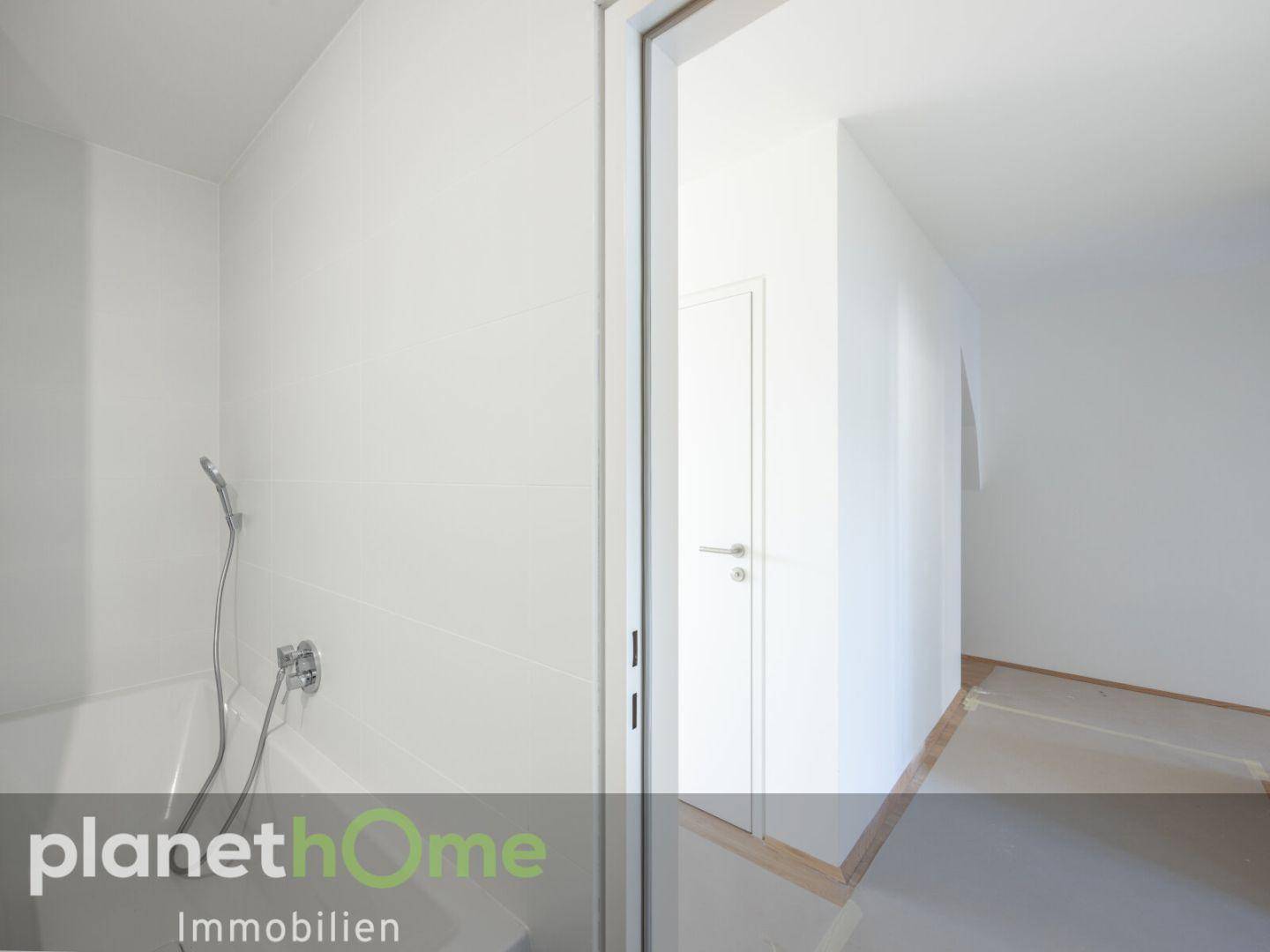 Modernes Badezimmer mit weißen Fliesen und Badewanne, angrenzend an einen hellen Flur.