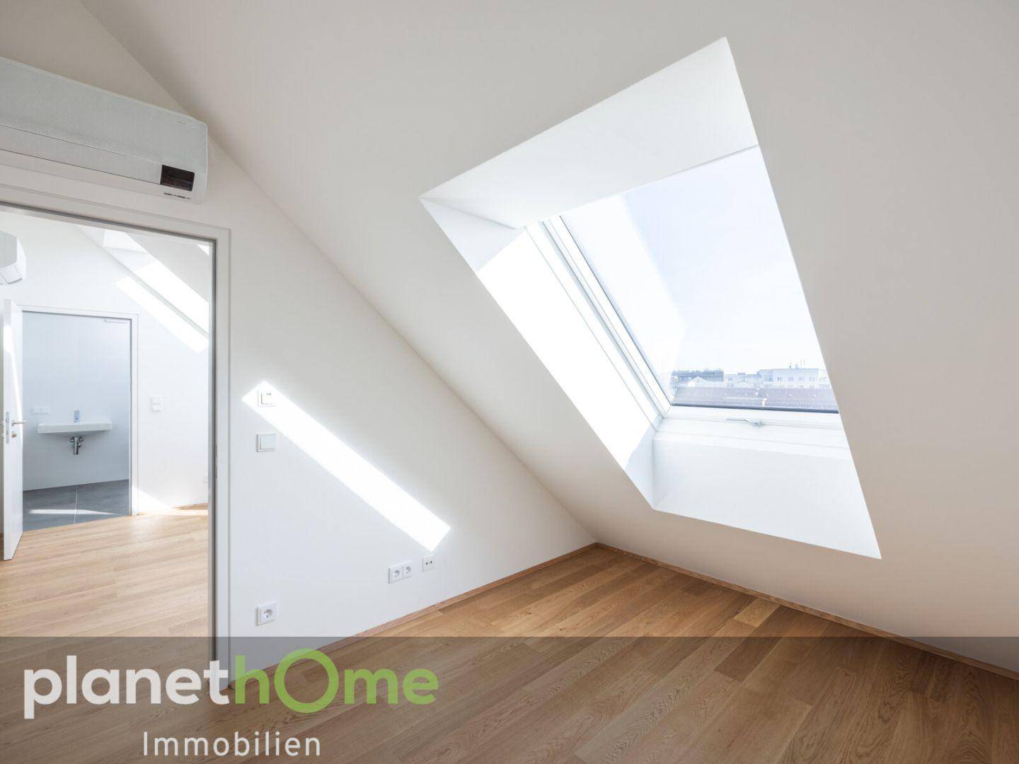 Helles Dachzimmer mit Holzboden, Dachschräge, Dachfenster und Klimaanlage.