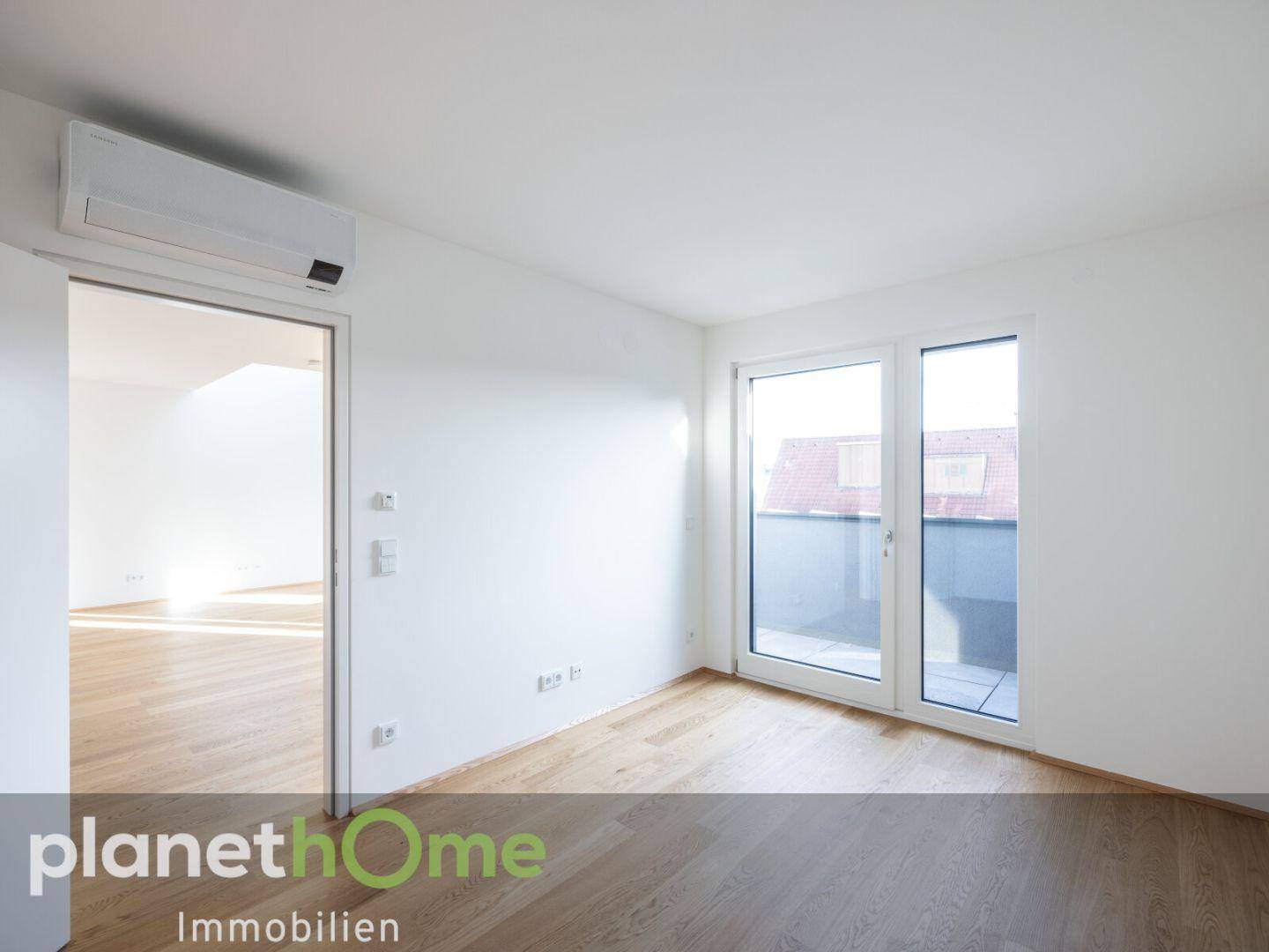 Lichtdurchflutetes Zimmer mit Parkettboden, Klimaanlage und Zugang zu einem Außenbereich.