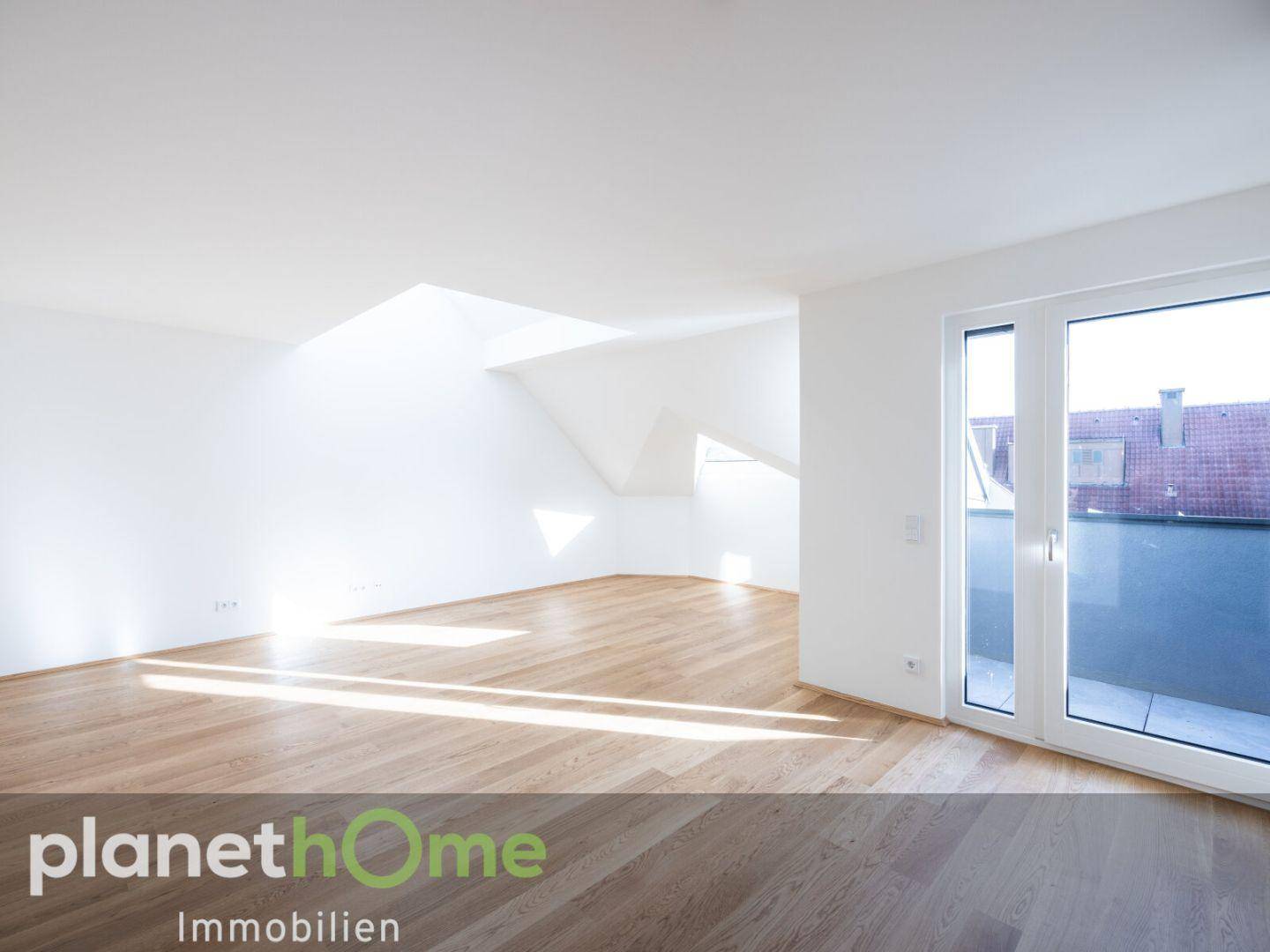 Heller Wohnraum mit Holzboden, Dachschrägen und großem Fenster mit Zugang zur Terrasse.