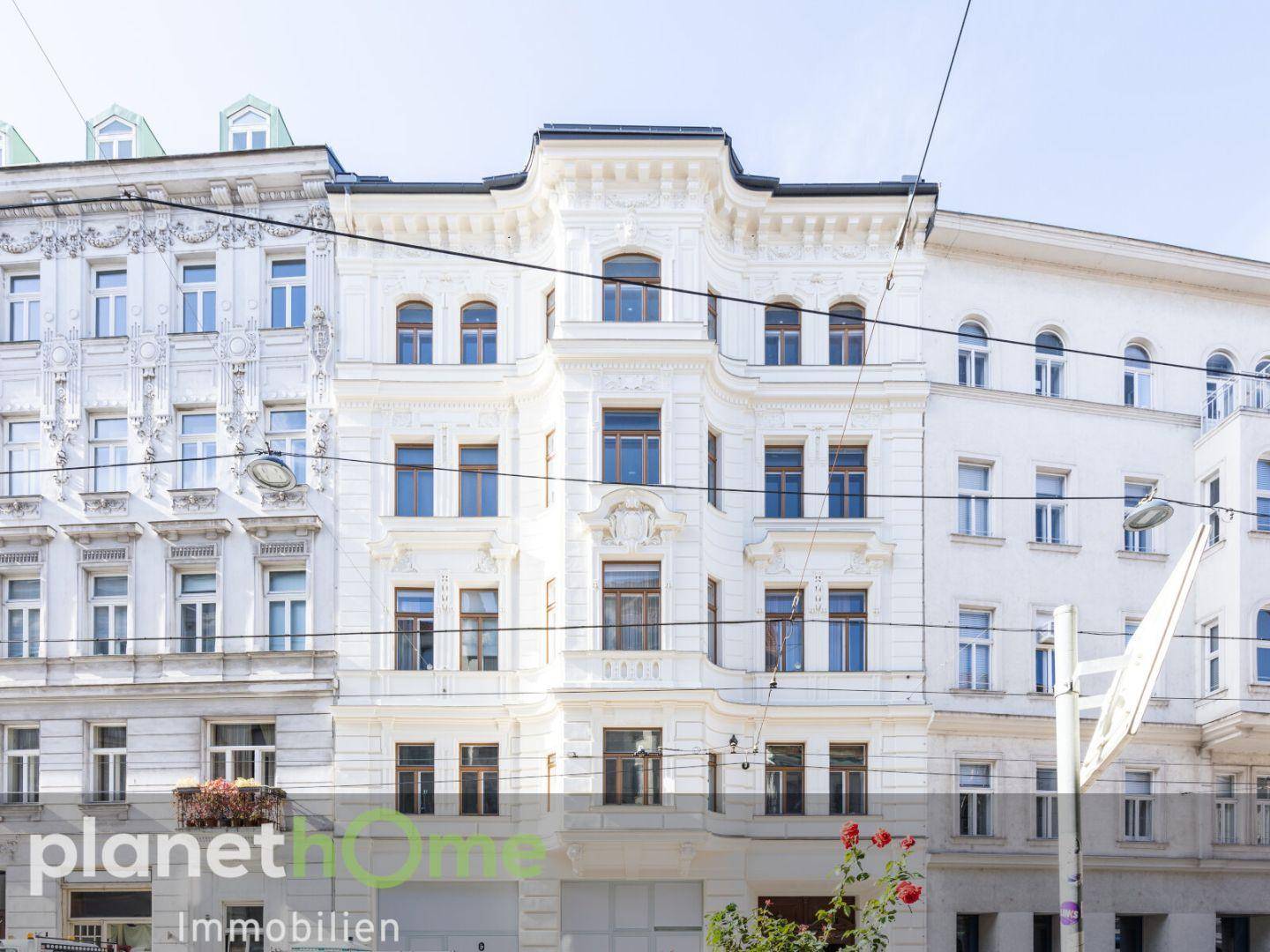 Historische Fassade eines Altbaus mit reich verzierten Details und großen Fenstern.
