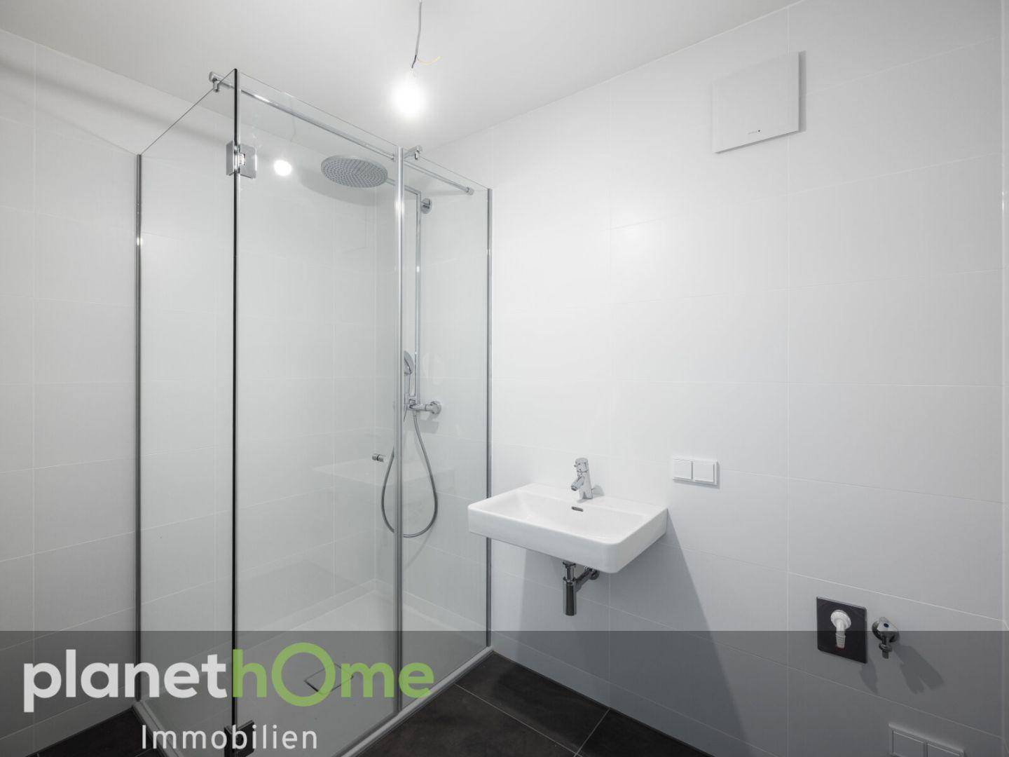 Modernes Badezimmer mit ebenerdiger Dusche, weiß gefliesten Wänden und dunklem Boden.