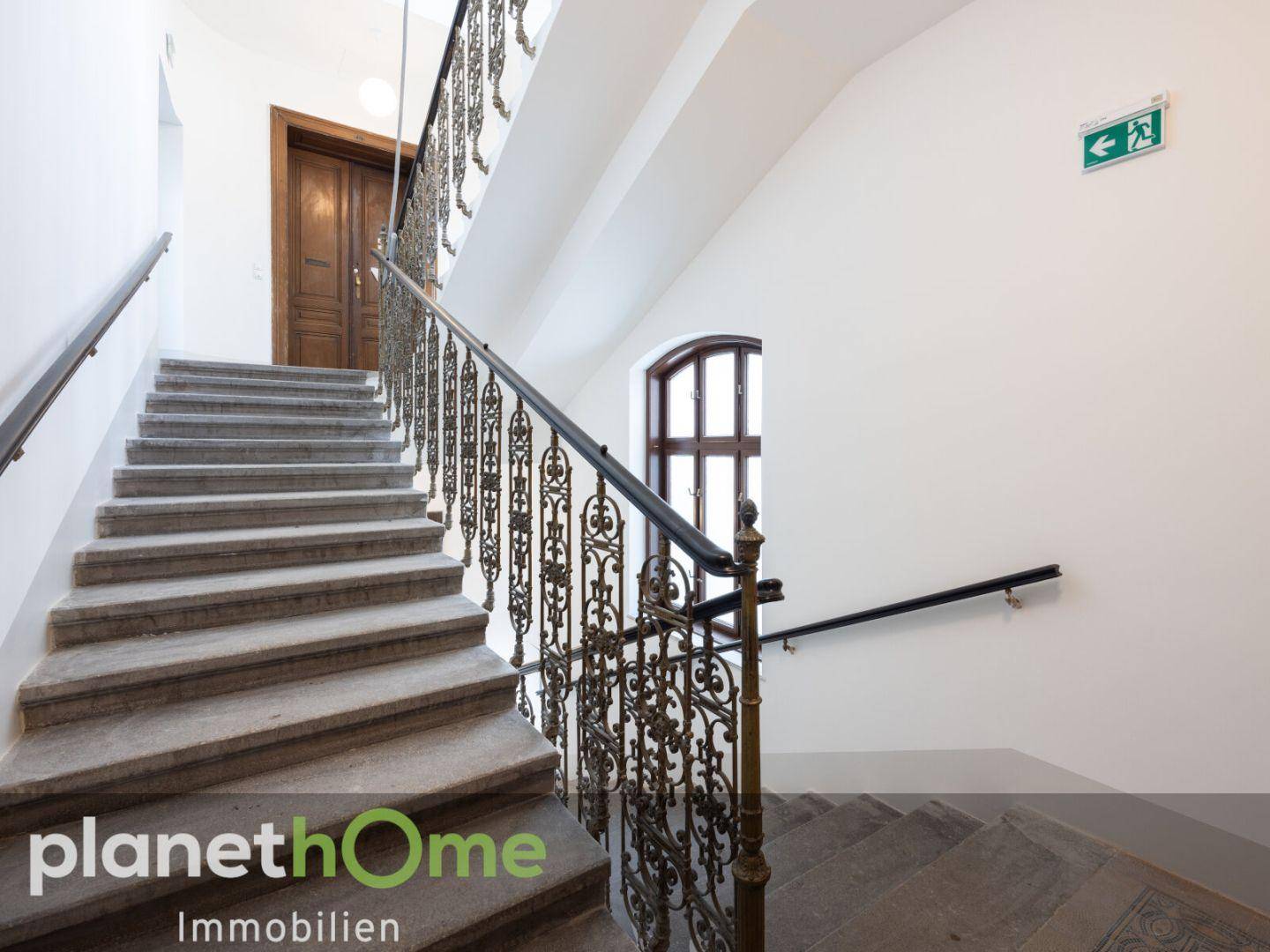 Elegantes Treppenhaus mit Steinstufen und kunstvollem schmiedeeisernem Geländer in einem Altbau.