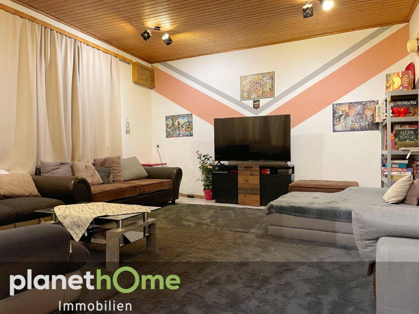 Gemütliches Wohnzimmer mit Holzbalkendecke, großem Fernseher und bequemen Sofas.