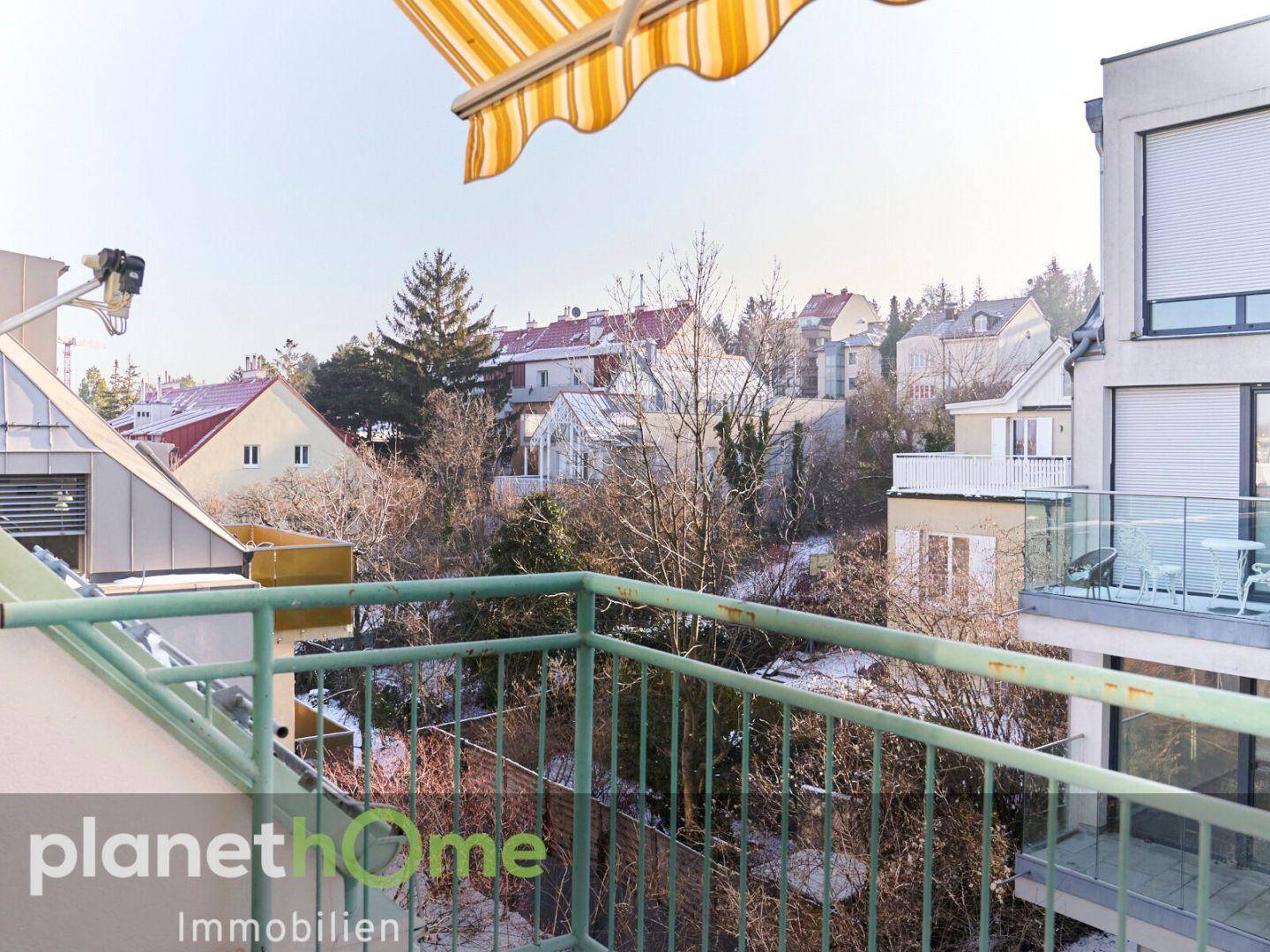 Balkon mit Markise und Blick auf die umliegenden Häuser und Bäume.