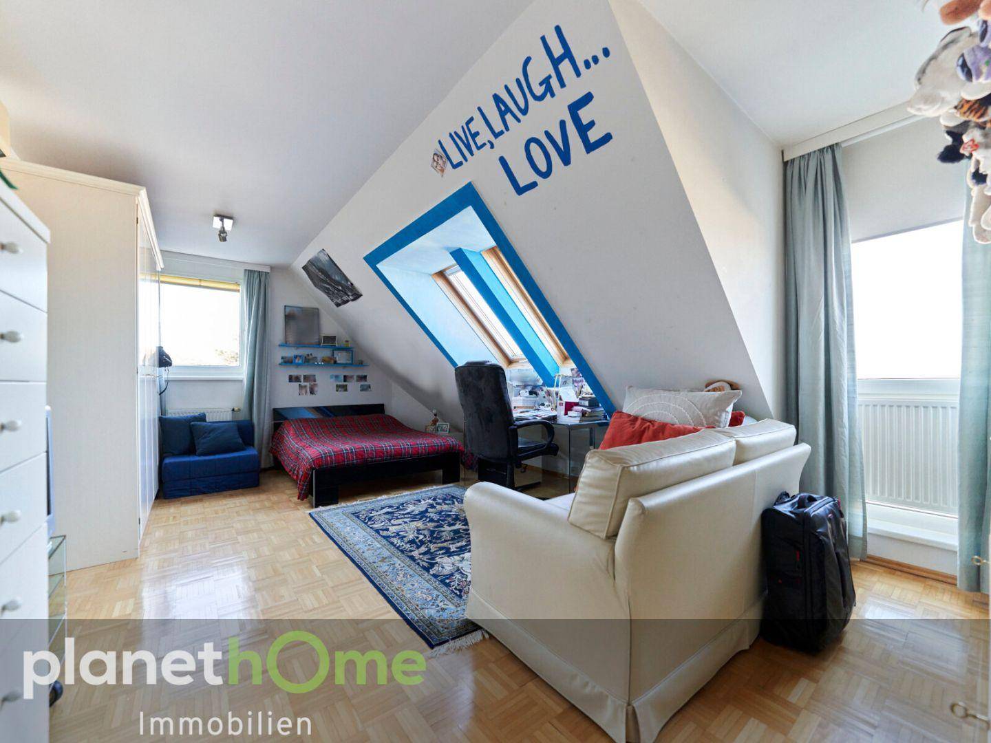Dachgeschosszimmer mit Bett, Schreibtisch, Sofa und Dachfenstern.