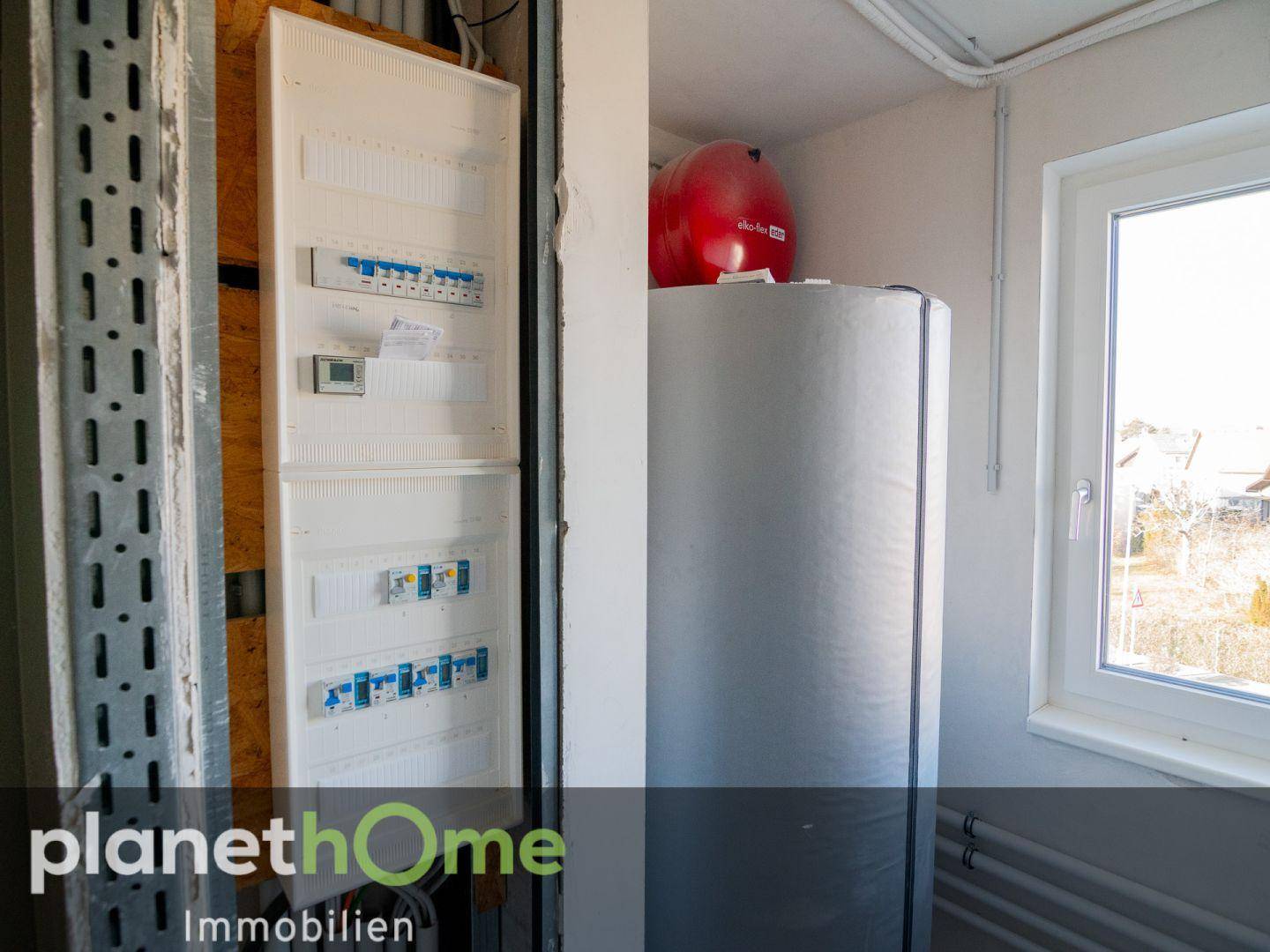 Technikraum mit Sicherungskasten, Warmwasserspeicher und Fenster.