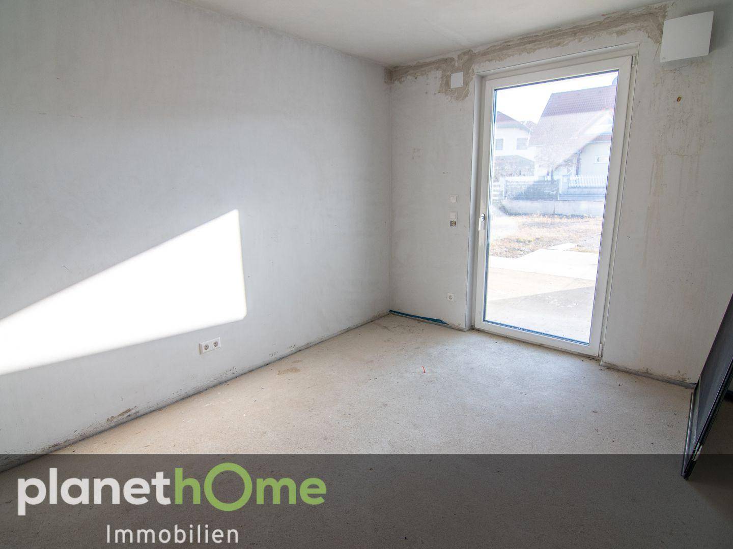 Rohbauzimmer mit großem Fenster und Zugang nach draußen, bereit für den Innenausbau.