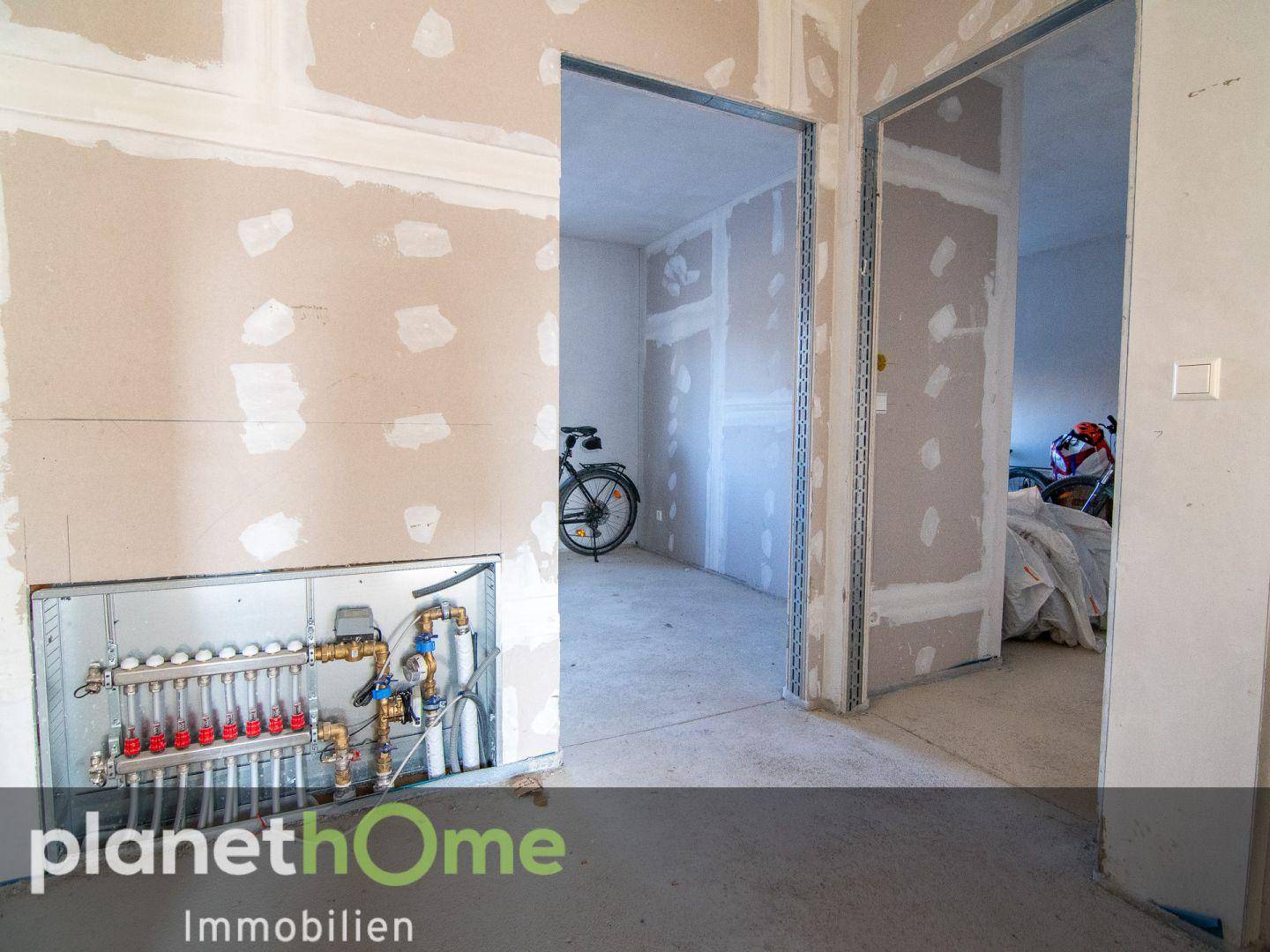 Innenraum im Rohbau mit sichtbarer Fußbodenheizungsverteilung und Trockenbauwänden.