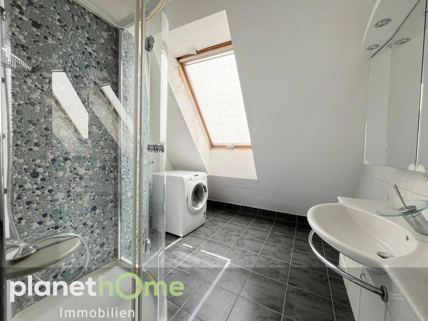 Modernes Badezimmer mit Dusche, Waschmaschine und Dachfenster unter einer Dachschräge.