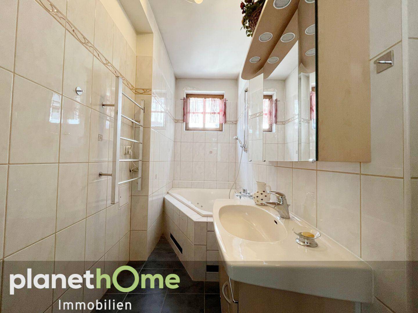Helles Badezimmer mit Eckbadewanne, Waschbecken und Spiegelschrank, komplett gefliest.
