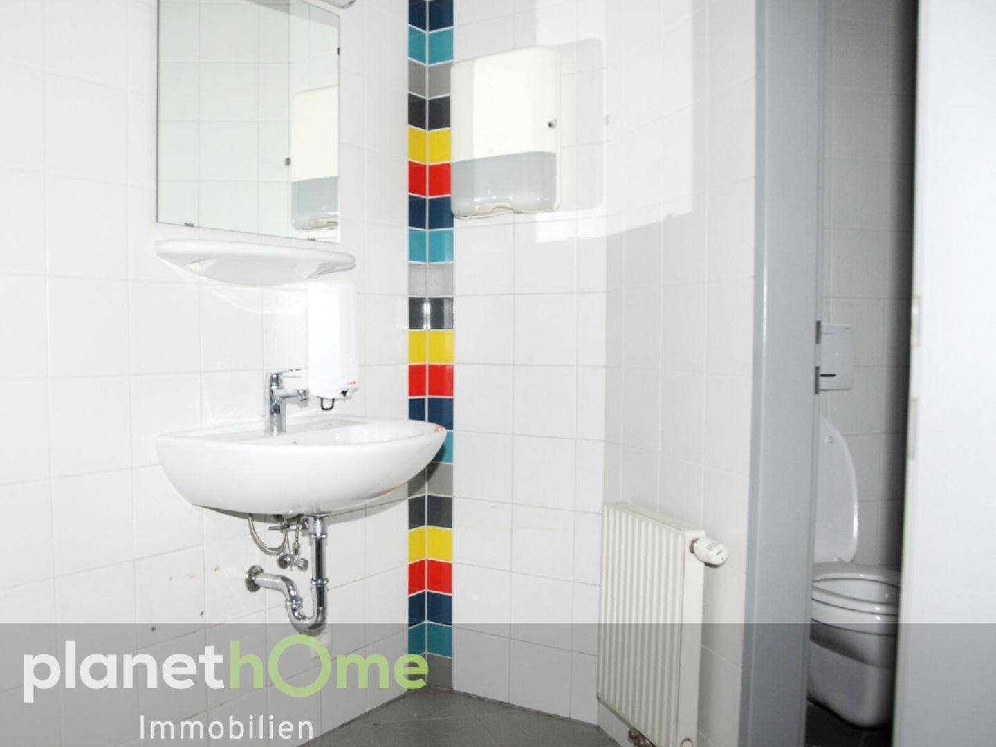 Funktionales WC mit Waschbecken, Spiegel, Heizkörper und einer farbigen Fliesenbordüre.