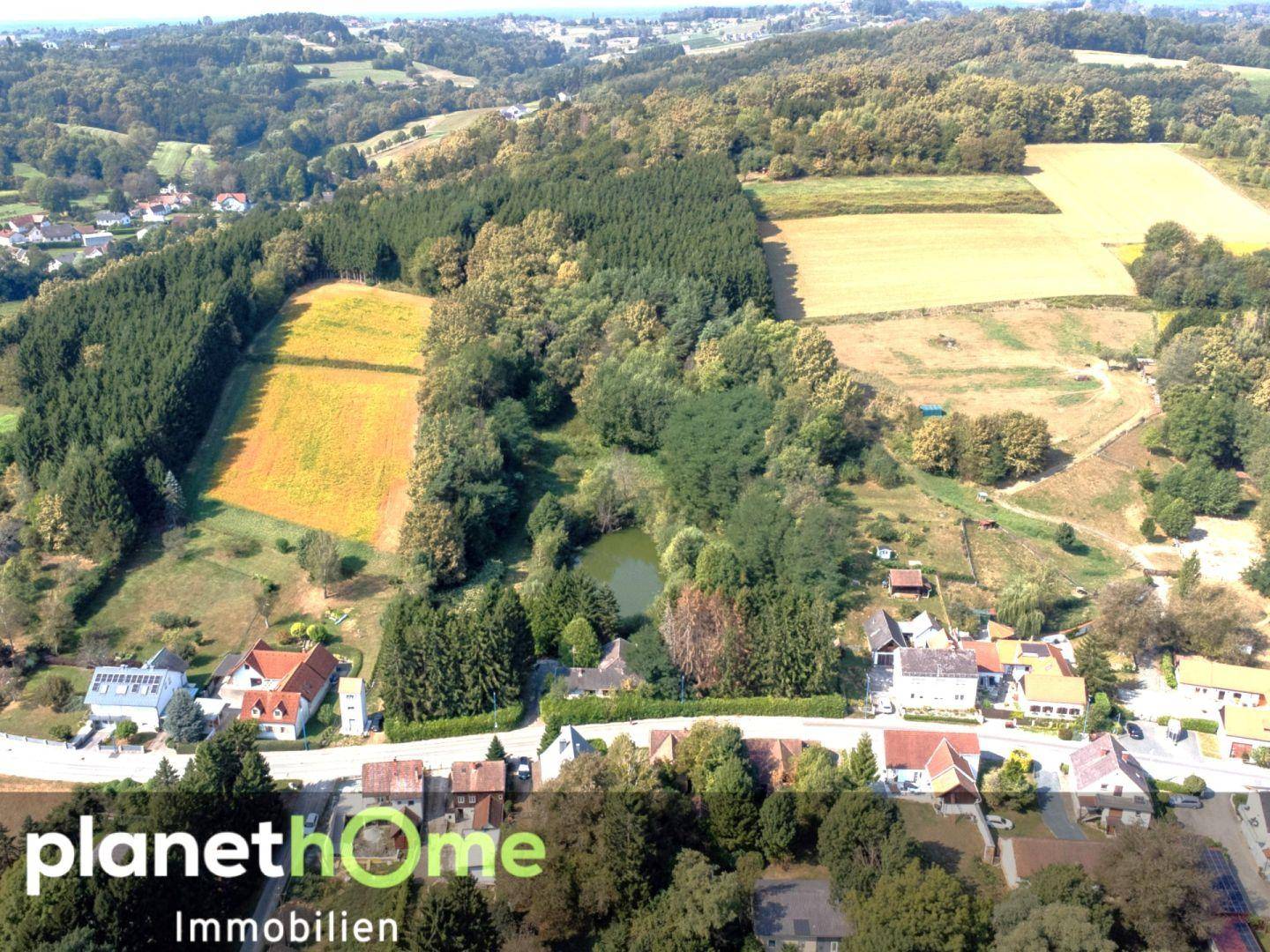 Weitläufige Luftaufnahme der grünen Landschaft mit Wohnbebauung und einem Teich.