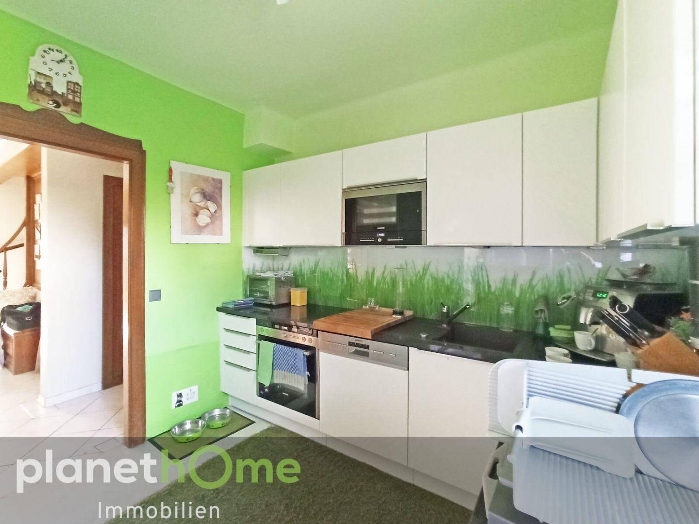 Moderne Küche mit weißen Schränken, dunkler Arbeitsplatte und grüner Wandgestaltung.
