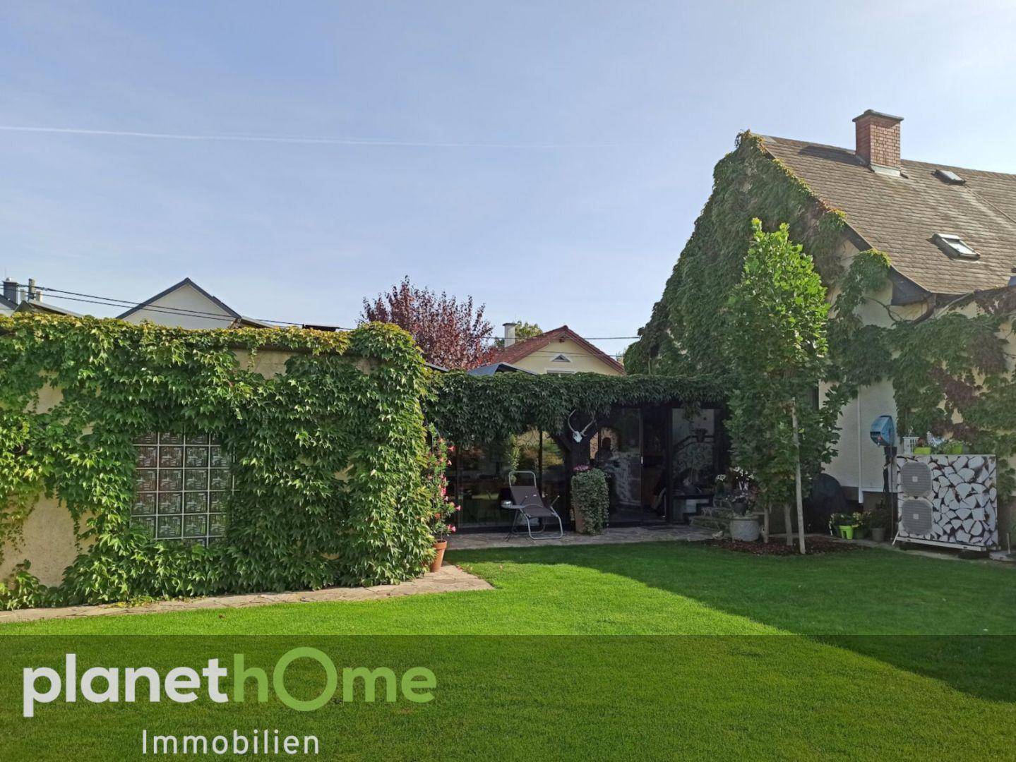 Grüner Gartenbereich mit überdachter Terrasse und Kletterpflanzen an der Hauswand.