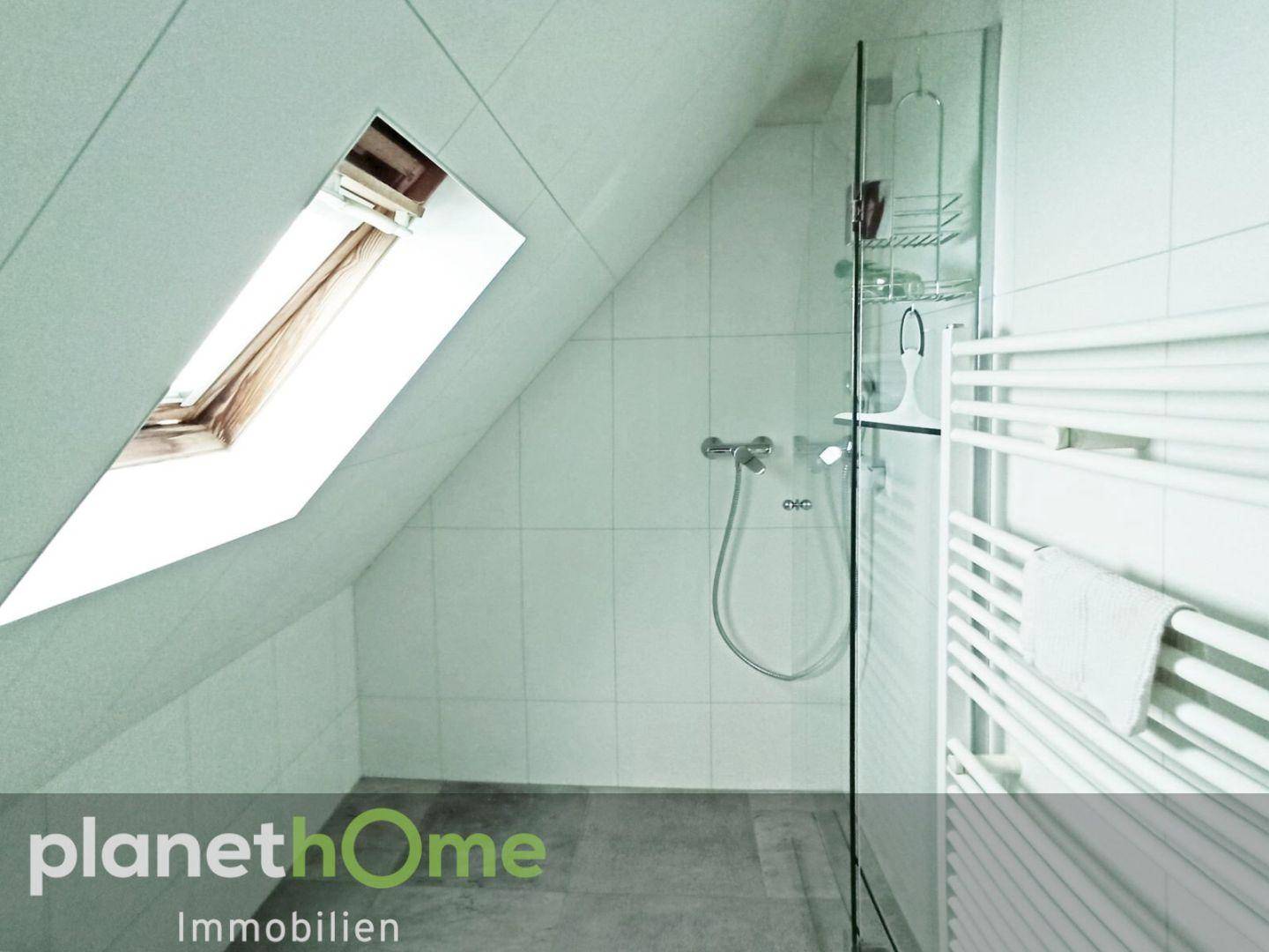 Helles Badezimmer im Dachgeschoss mit Dusche, Dachfenster und Handtuchheizkörper.