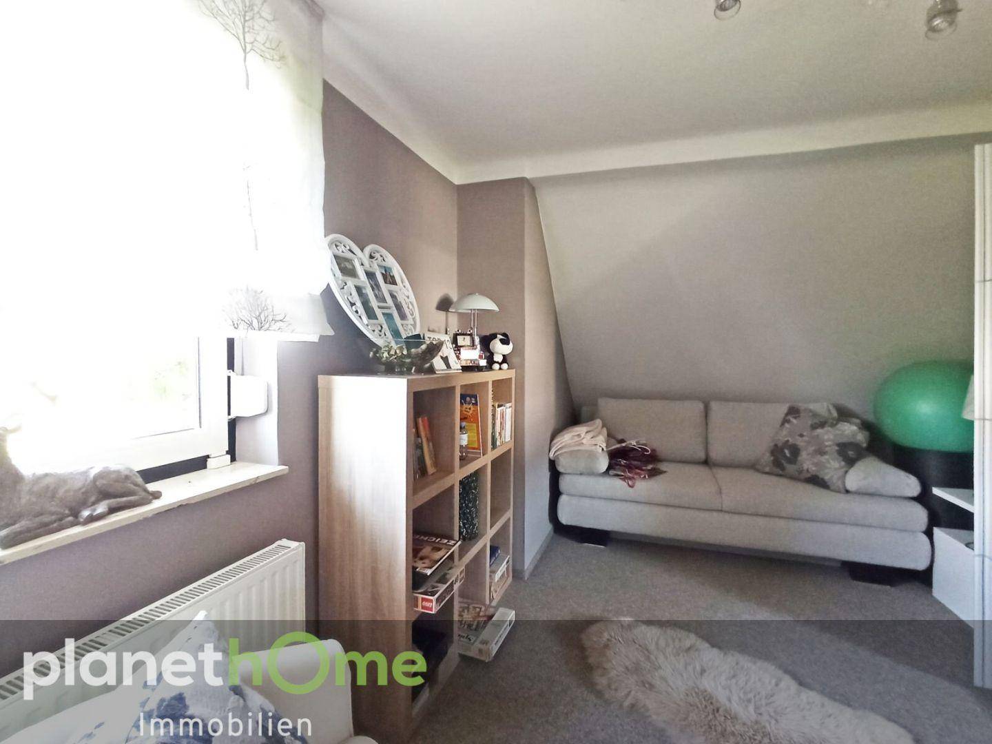Dachzimmer mit Schräge, Sofa und Regal, ideal als Gäste- oder Kinderzimmer.