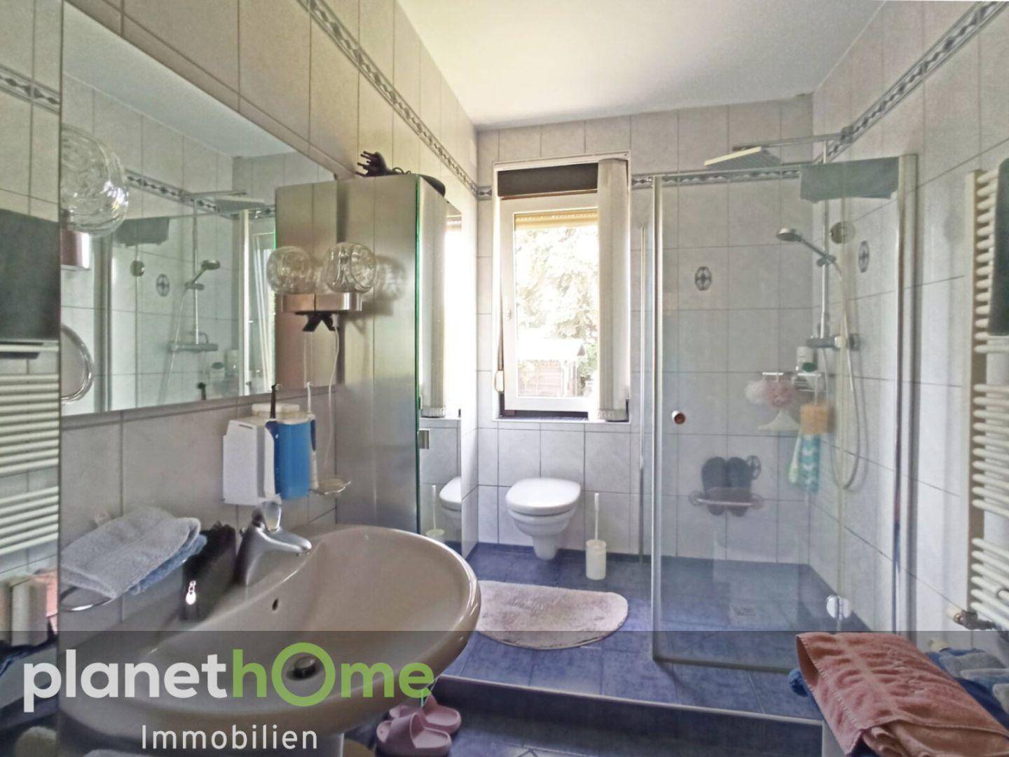 Gefliestes Badezimmer mit Dusche, Waschbecken, WC und Fenster.