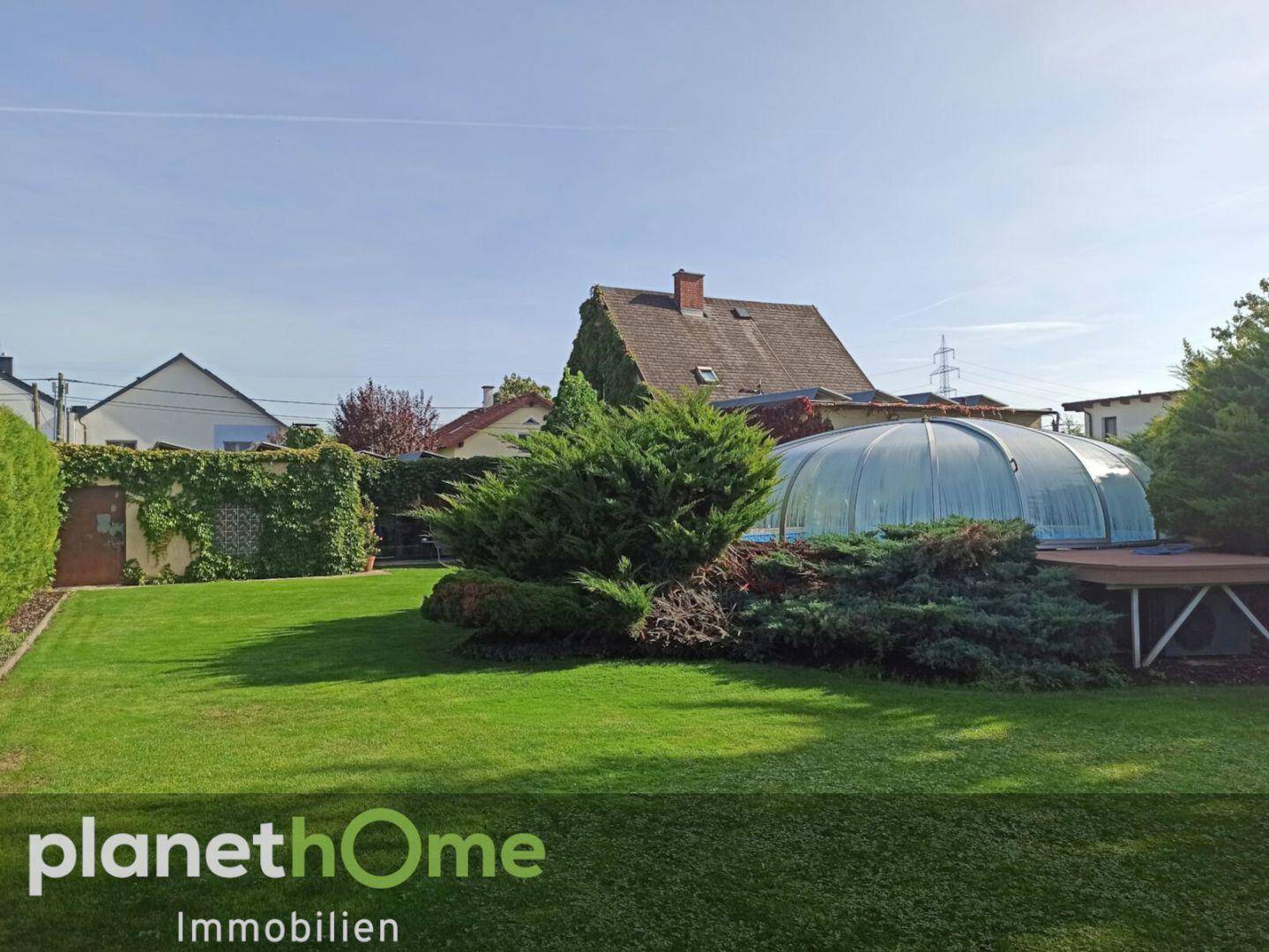 Großer Garten mit Rasenfläche und einem überdachten Swimmingpool im Hintergrund.