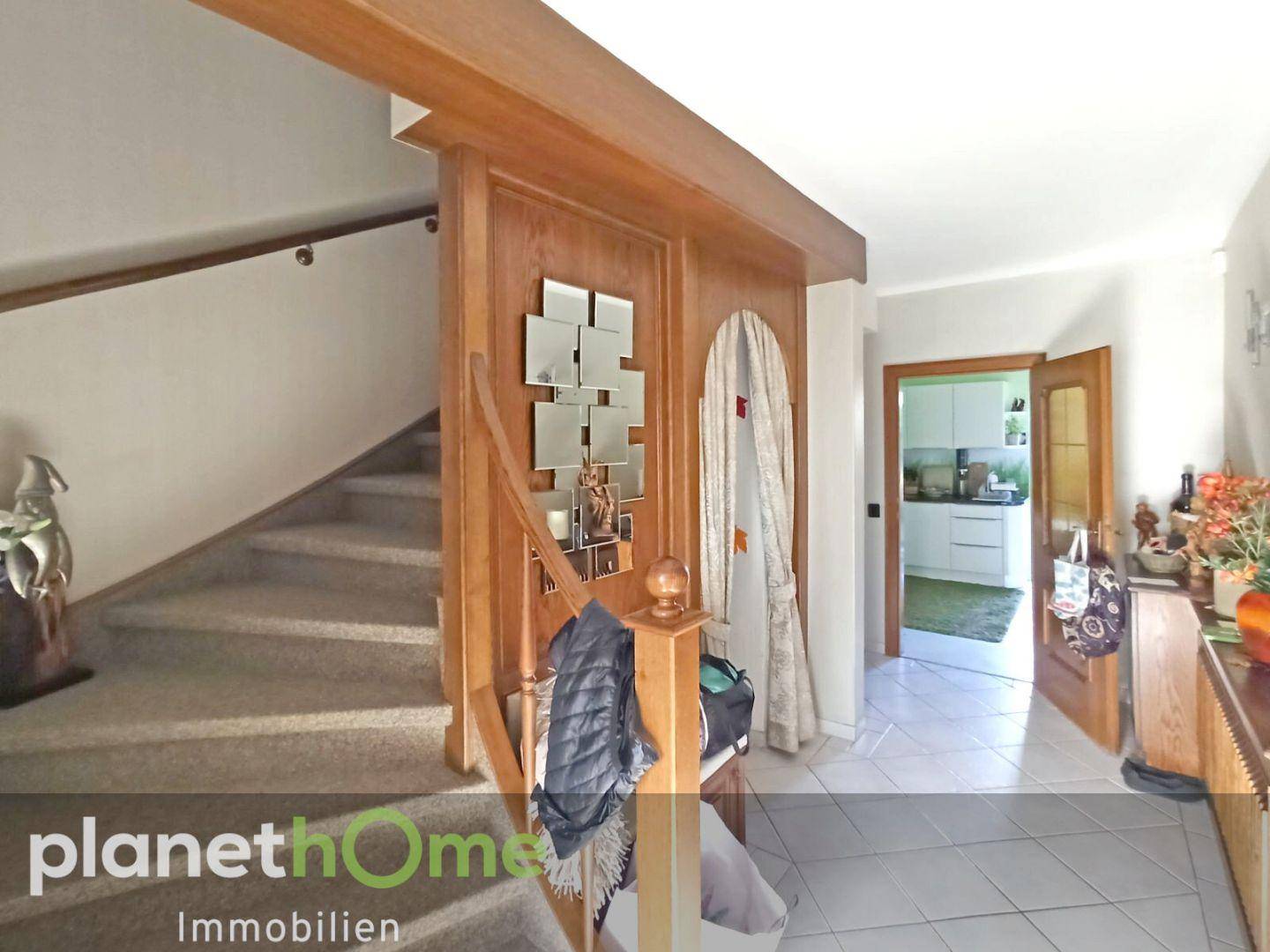 Geräumiger Eingangsbereich mit Holzvertäfelung, Teppichtreppe und Blick in die Küche.