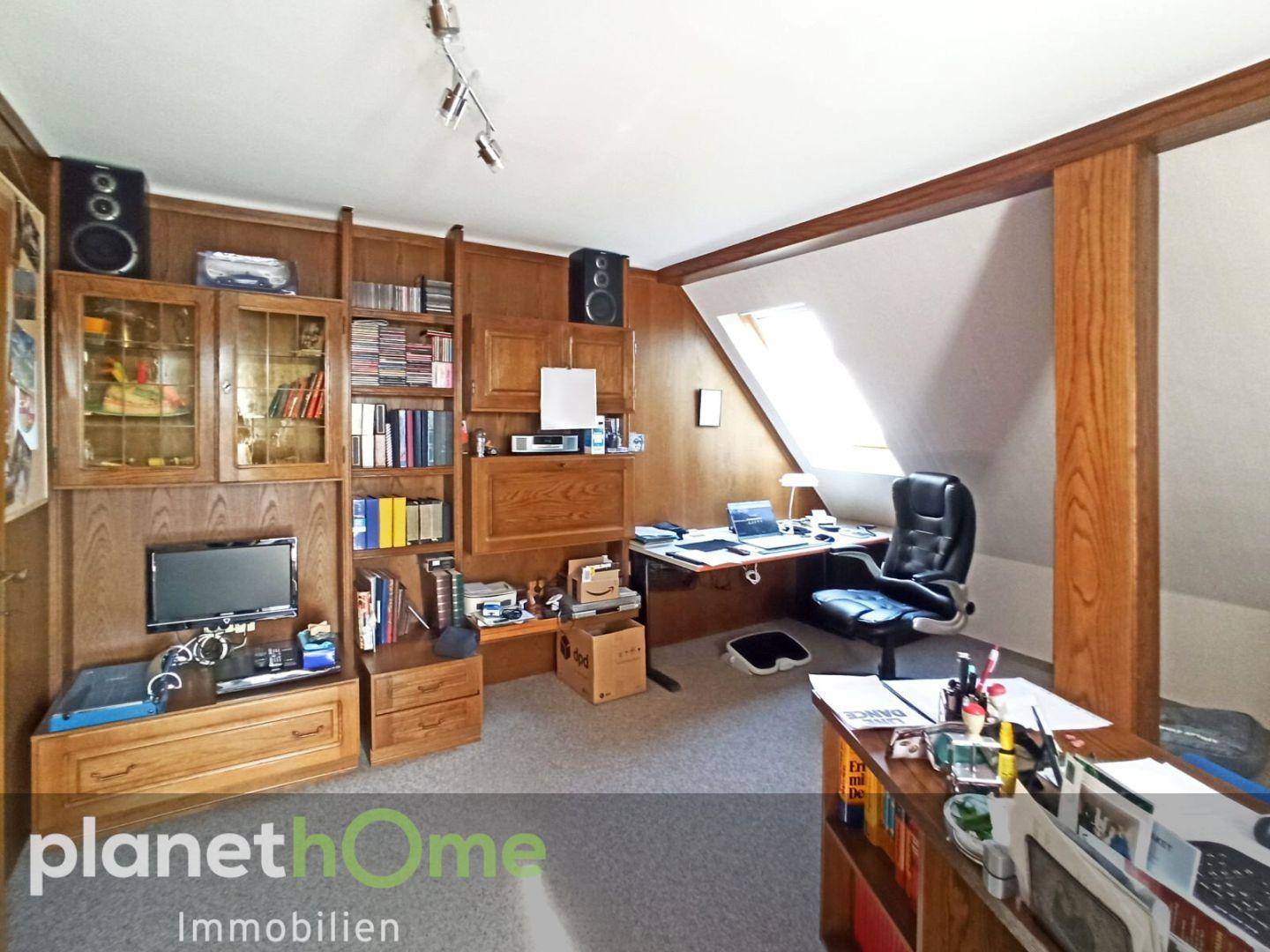 Geräumiges Büro im Dachgeschoss mit Holzvertäfelung, Bücherregalen und Schreibtisch.
