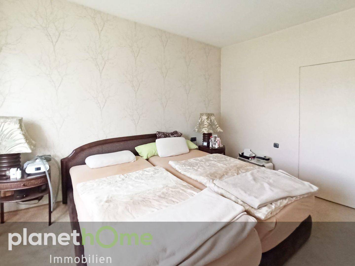 Helles Schlafzimmer mit Doppelbett, Nachttischen und gemusterter Tapete.