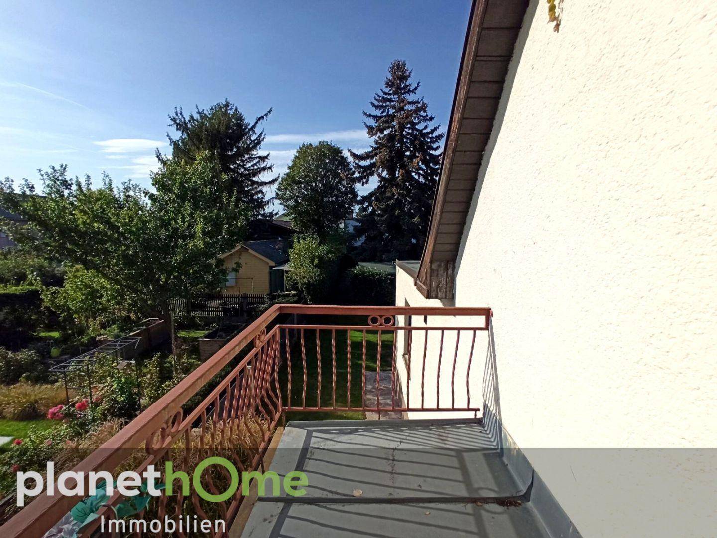 Balkon mit schmiedeeisernem Geländer und Blick auf den Garten und Bäume.