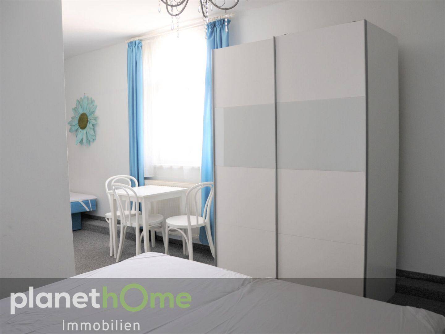 Freundliches Schlafzimmer mit weißem Kleiderschrank, kleinem Tisch und blauen Vorhängen.