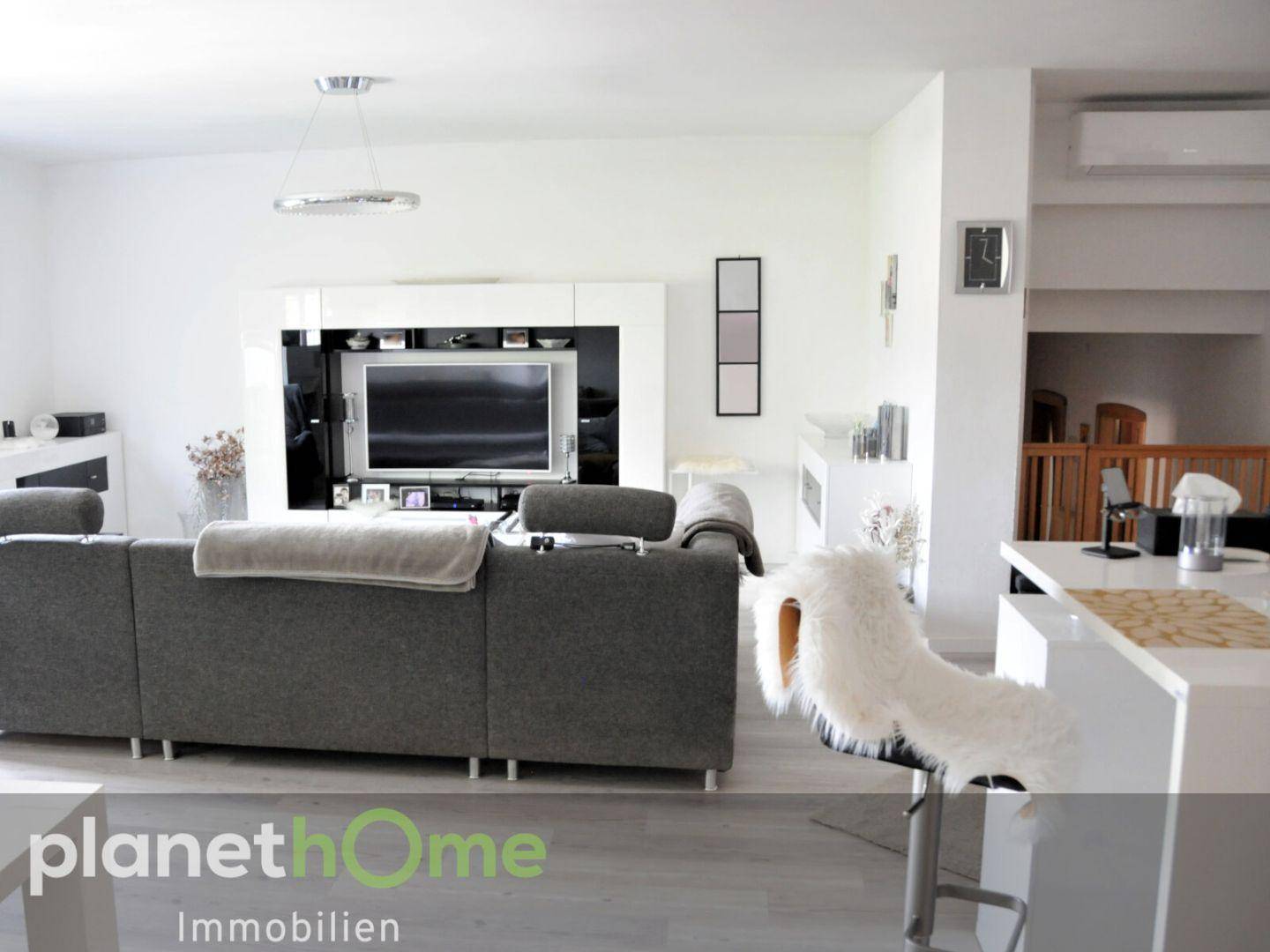 Heller Wohnbereich mit großem Sofa, Fernseher und moderner Einrichtung.