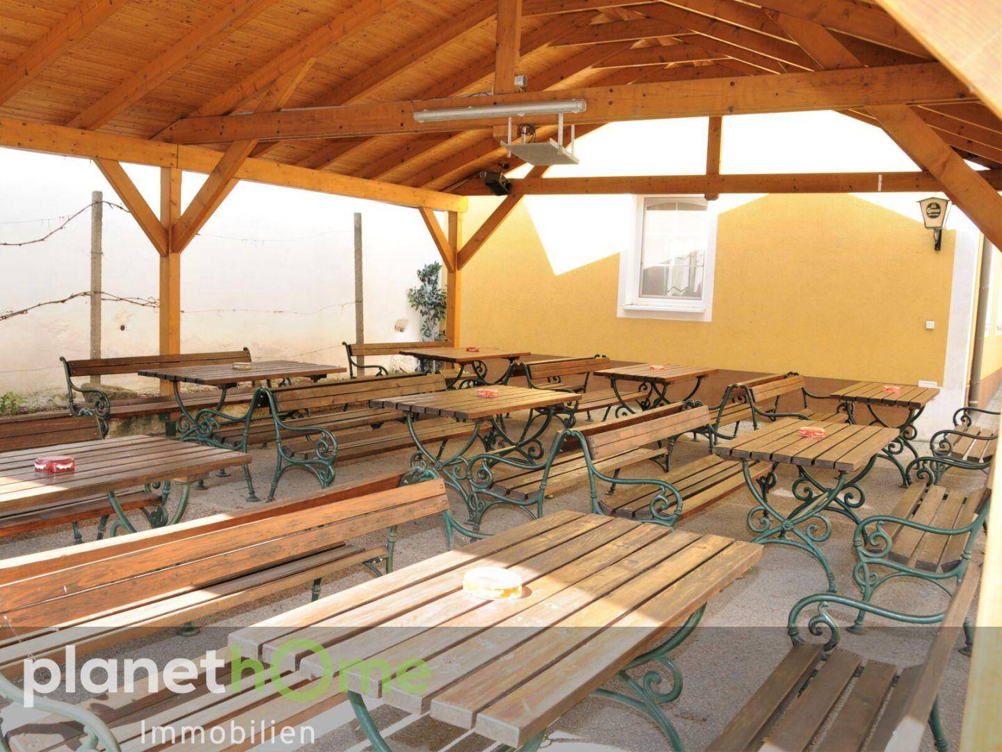 Überdachte Außenterrasse mit Holzdach und rustikalen Biertischen, ideal für gesellige Runden.