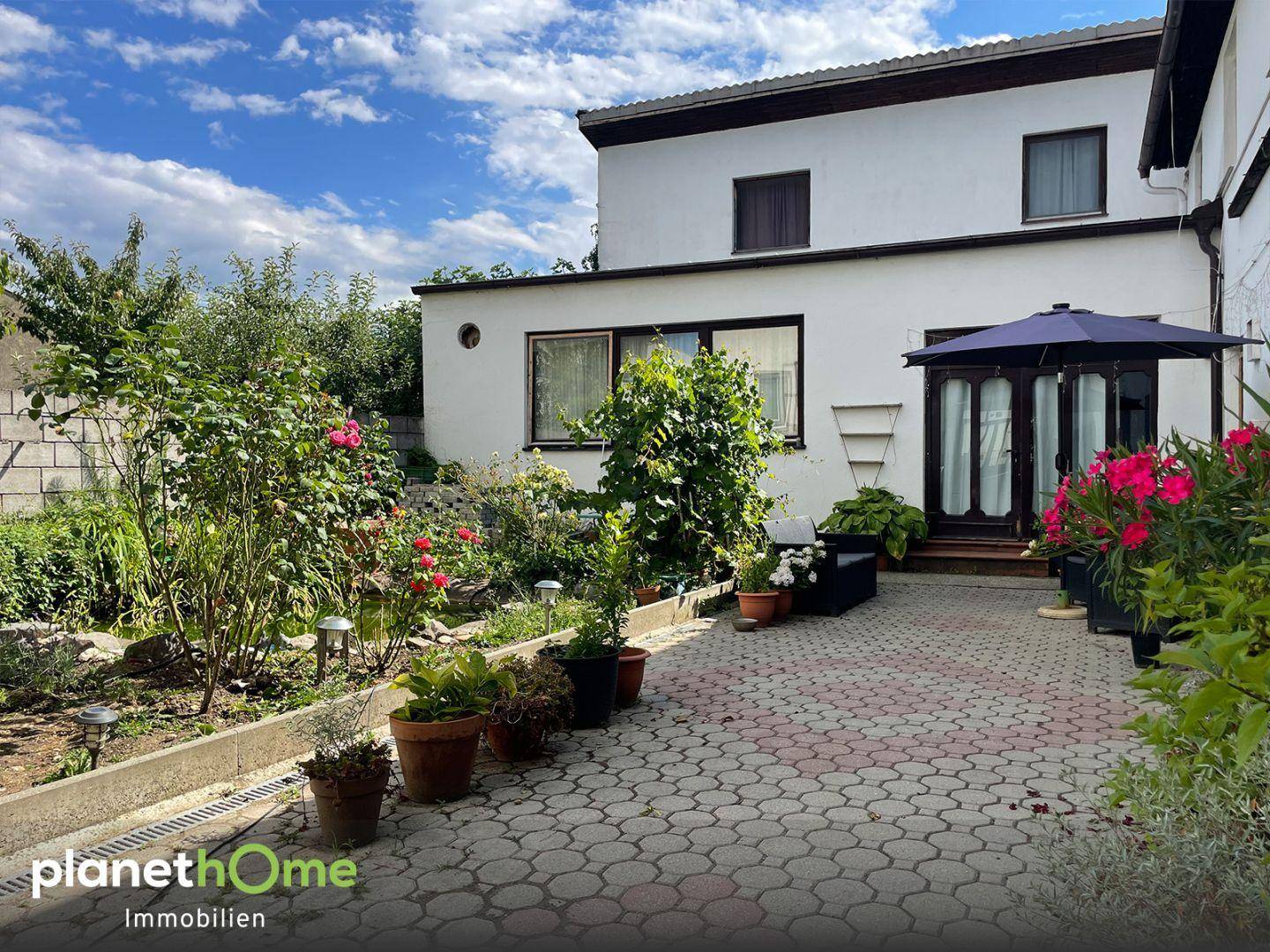 Heller Außenbereich mit gepflasterter Terrasse, üppigem Grün und Gartenbeeten.