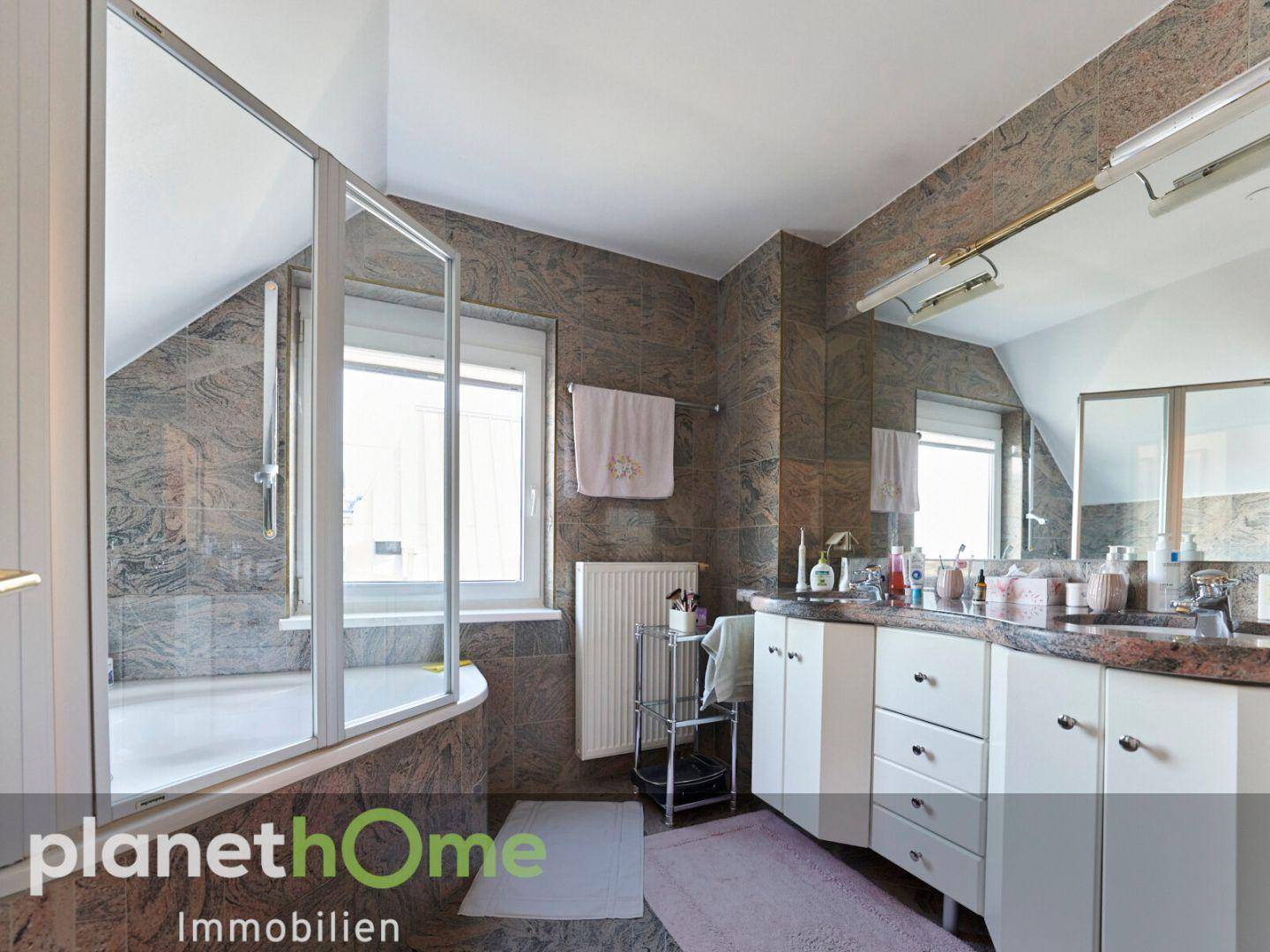 Badezimmer mit Doppelwaschbecken, Badewanne mit Duschabtrennung und Fenster unter Dachschräge.