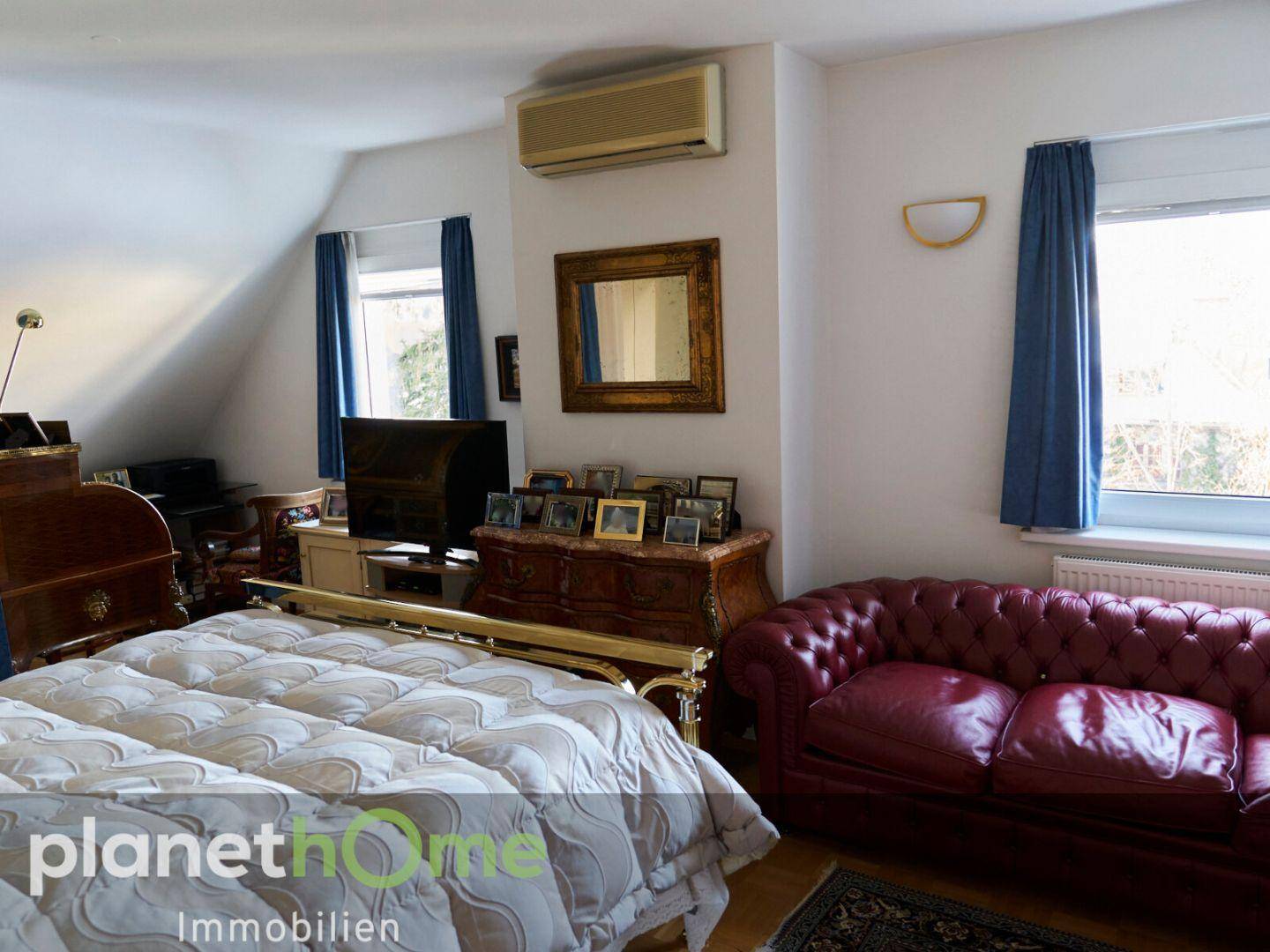Schlafzimmer mit klassischem Bett, rotem Ledersofa und Klimaanlage unter Dachschrägen.