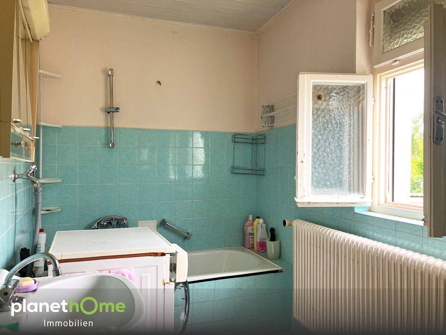 Badezimmer mit blauen Fliesen, einer Badewanne, Dusche und einem Fenster für natürliche Belüftung.