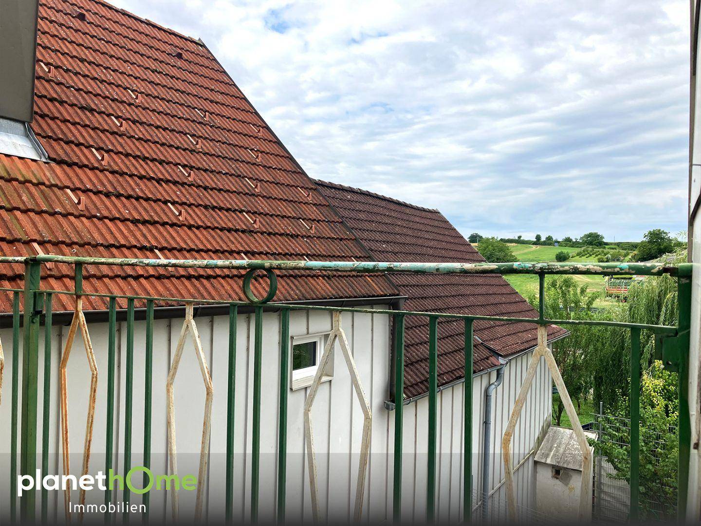 Blick vom Balkon auf das Ziegeldach des Hauses und die grüne Umgebung.