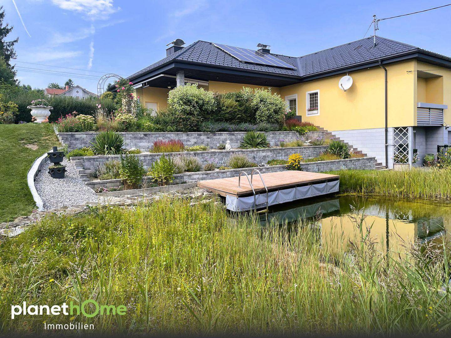 Ansicht des Hauses mit Naturteich, Holzsteg und terrassiertem Gartenbereich.