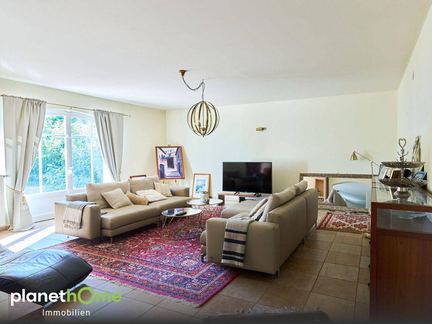 Helles Wohnzimmer mit beigen Sofas, großem Teppich und Zugang zum Garten.