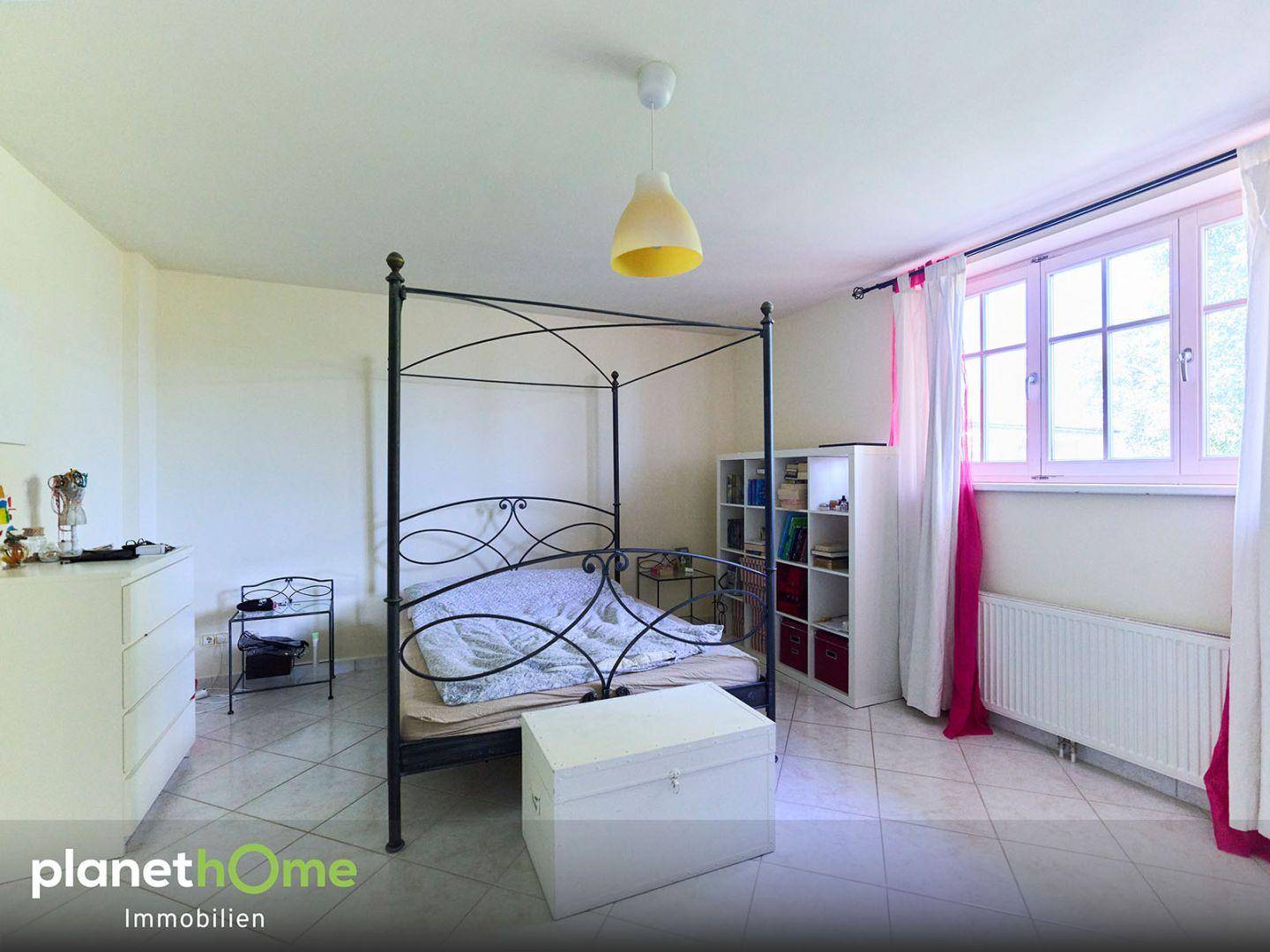 Helles Schlafzimmer mit Himmelbett, Fliesenboden und farbigen Vorhängen.