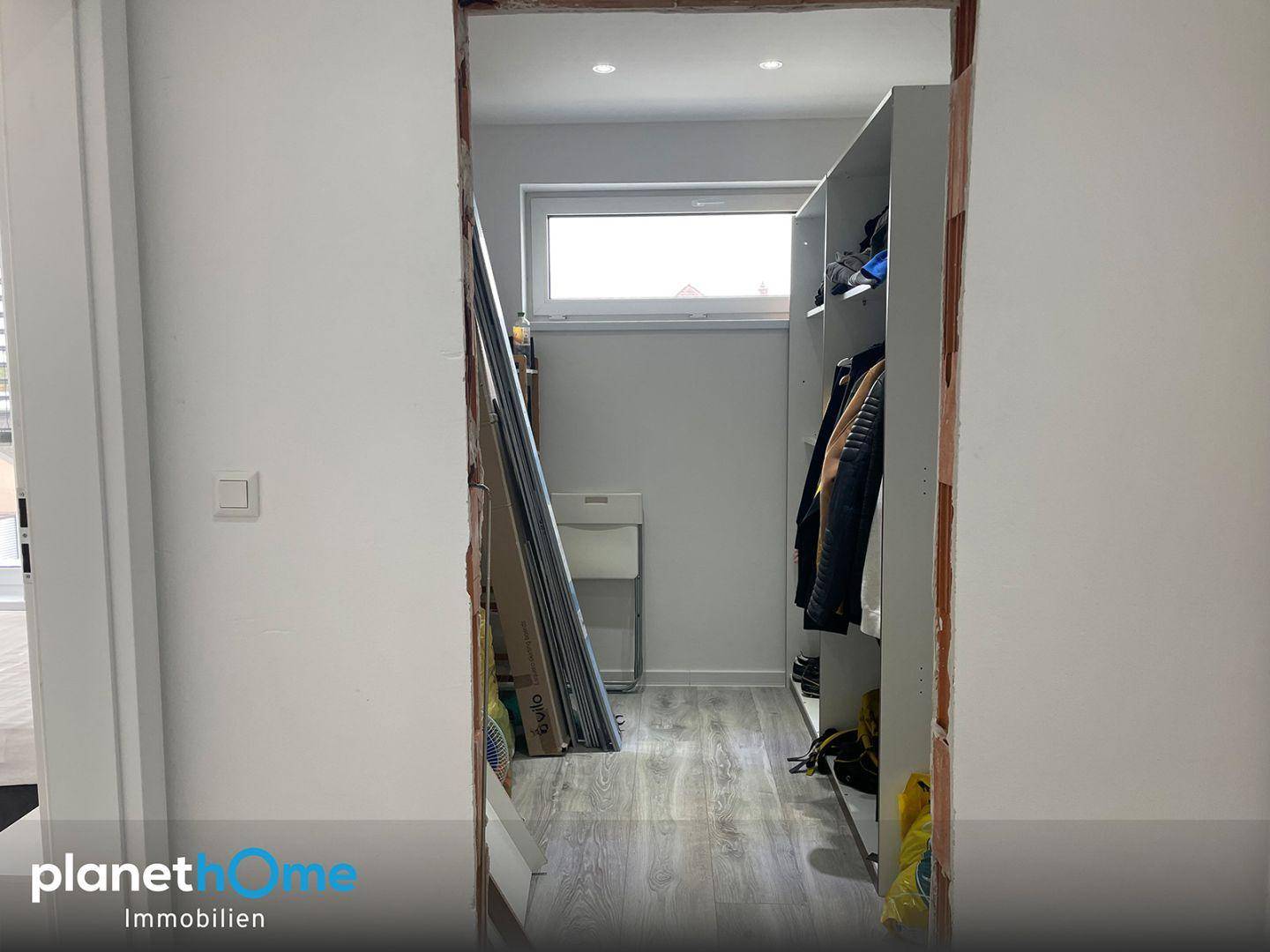 Abstellraum oder begehbarer Kleiderschrank mit Fenster und Regalsystem im Rohbauzustand.